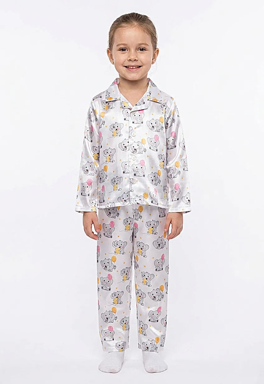 A smiling young girl wearing a white satin night suit featuring a cute grey elephant and colorful balloon print.
