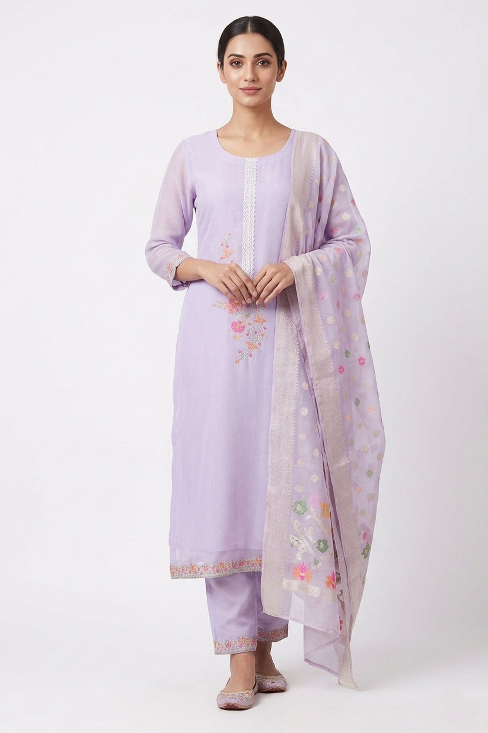 A woman modeling a lavender sheer organza salwar suit featuring floral embroidery, a lace-trimmed neck, and a matching organza dupatta with a wide silver border.