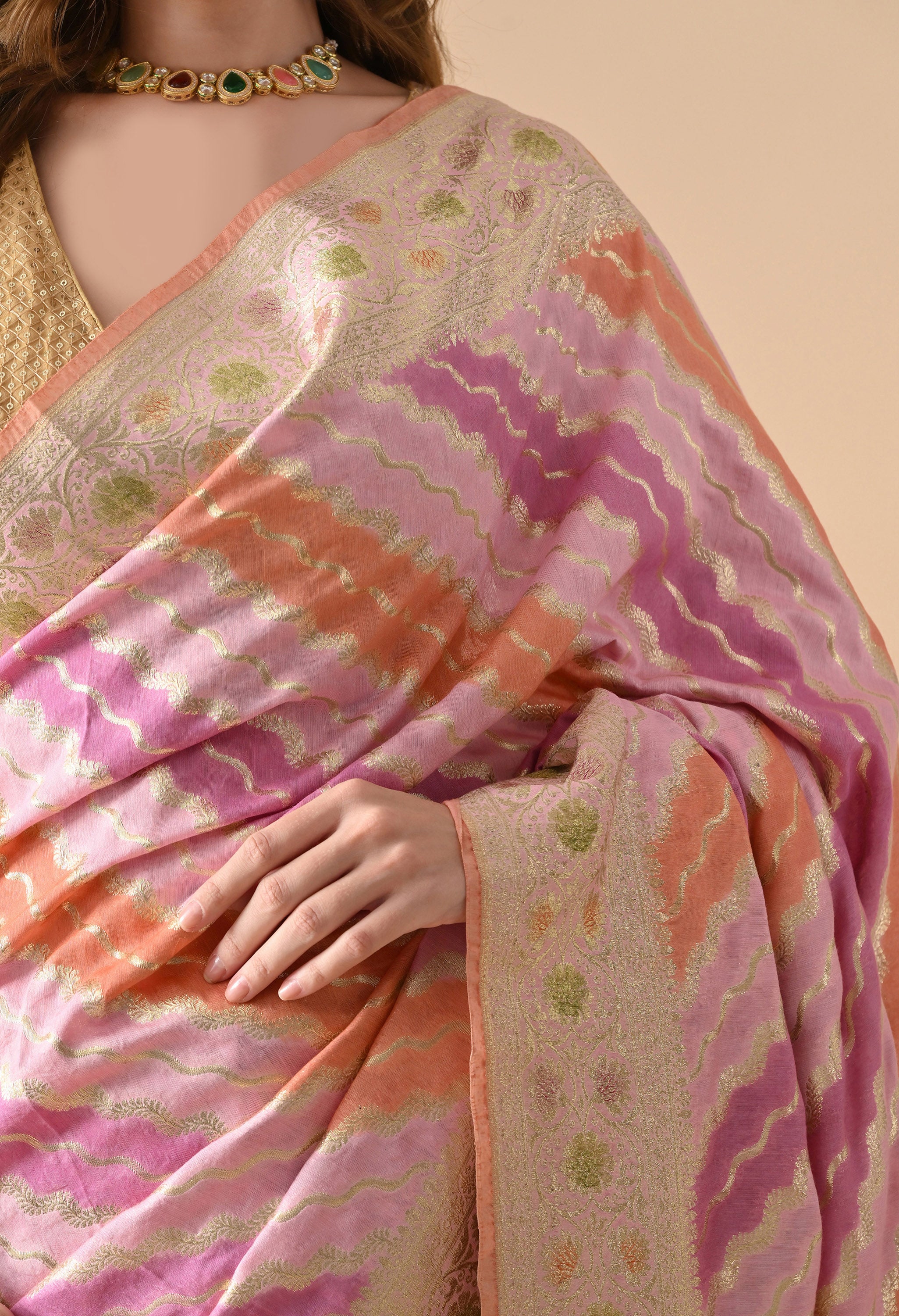 A detailed close-up of the Rangkat work on a Banarasi silk saree. The image showcases the precision of the gold zari weaving that traces the edges of the pink, purple, and orange wavy stripes. The intricate floral motifs on the border and the delicate texture of the silk are emphasized, highlighting the luxury craftsmanship of the piece.