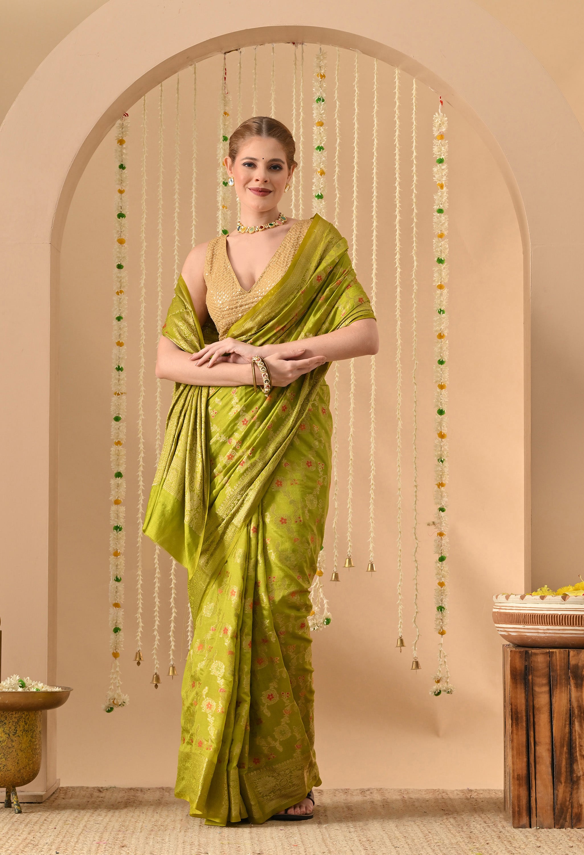 A model wearing a luxury lime-green Banarasi silk saree from The Weavers Shop by Raavi. The saree features exquisite Tilfi weaving, showcasing intricate floral motifs crafted with multi-coloured zari threads. The design includes a heavy gold zari border and is paired with a sleeveless gold sequined blouse, highlighting the traditional craftsmanship and rich texture of the silk.