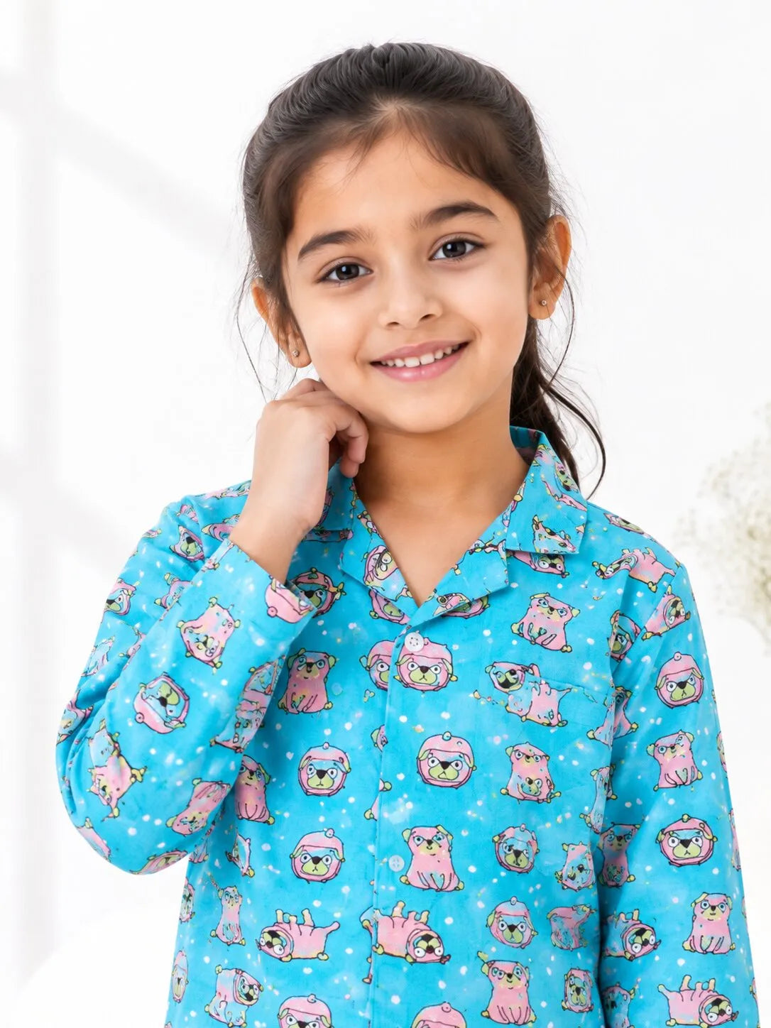 A young child wearing a turquoise cotton night suit with a pink puppy print and a button-front top.