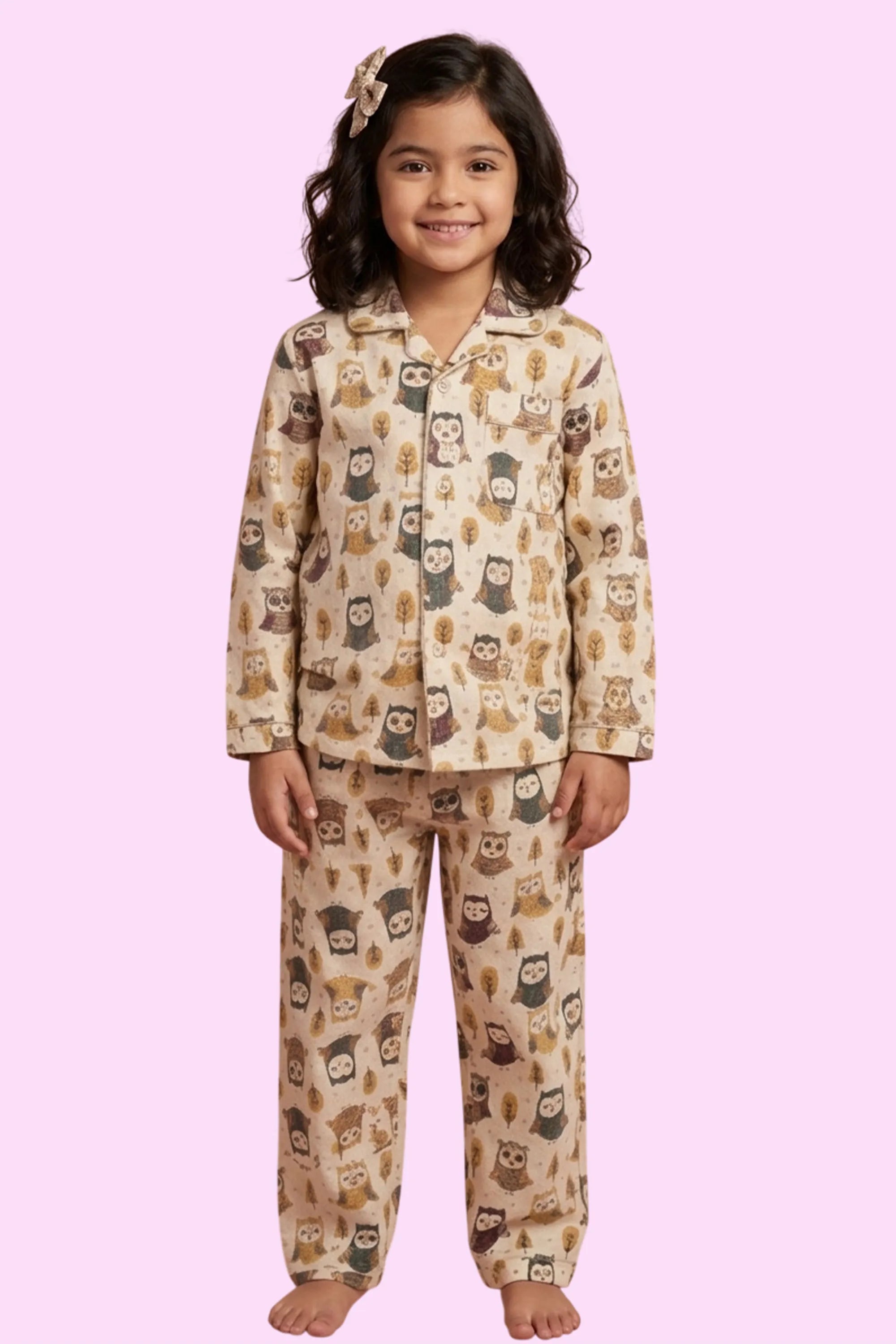 young girl wearing a cream-colored, long-sleeved pajama set featuring an all-over brown owl and tree branch print. The night suit is made of 100% pure cotton and includes a button-down shirt with a notched collar and matching straight-leg trousers.