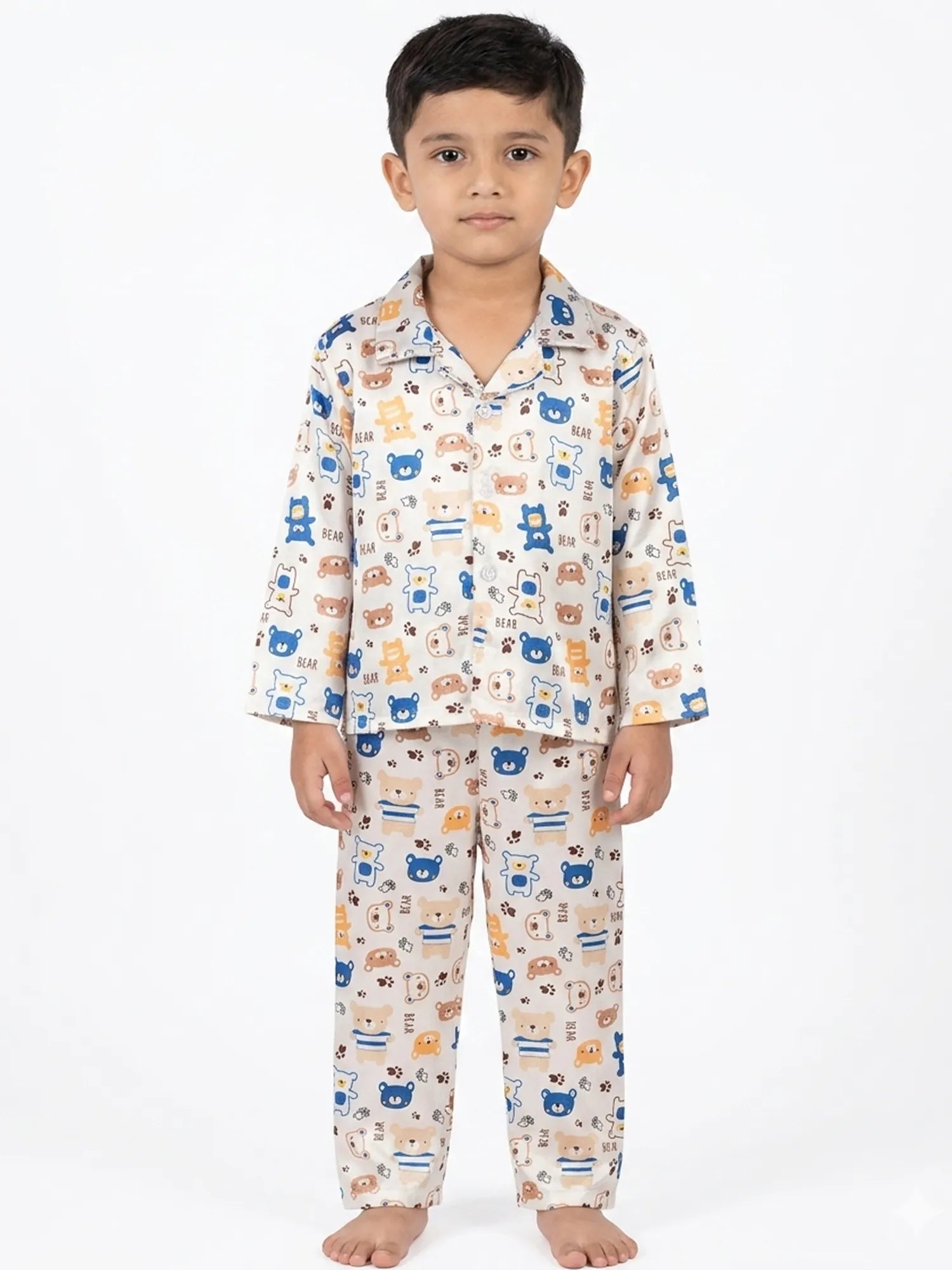 A young boy sitting cross-legged wearing a white satin night suit with a blue and brown bear print.
