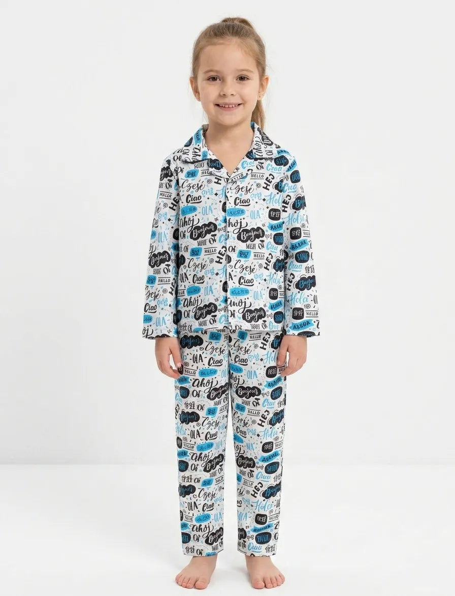 A young girls standing against a white background wearing a white satin night suit with a blue and black multilingual "Hello" typography print.