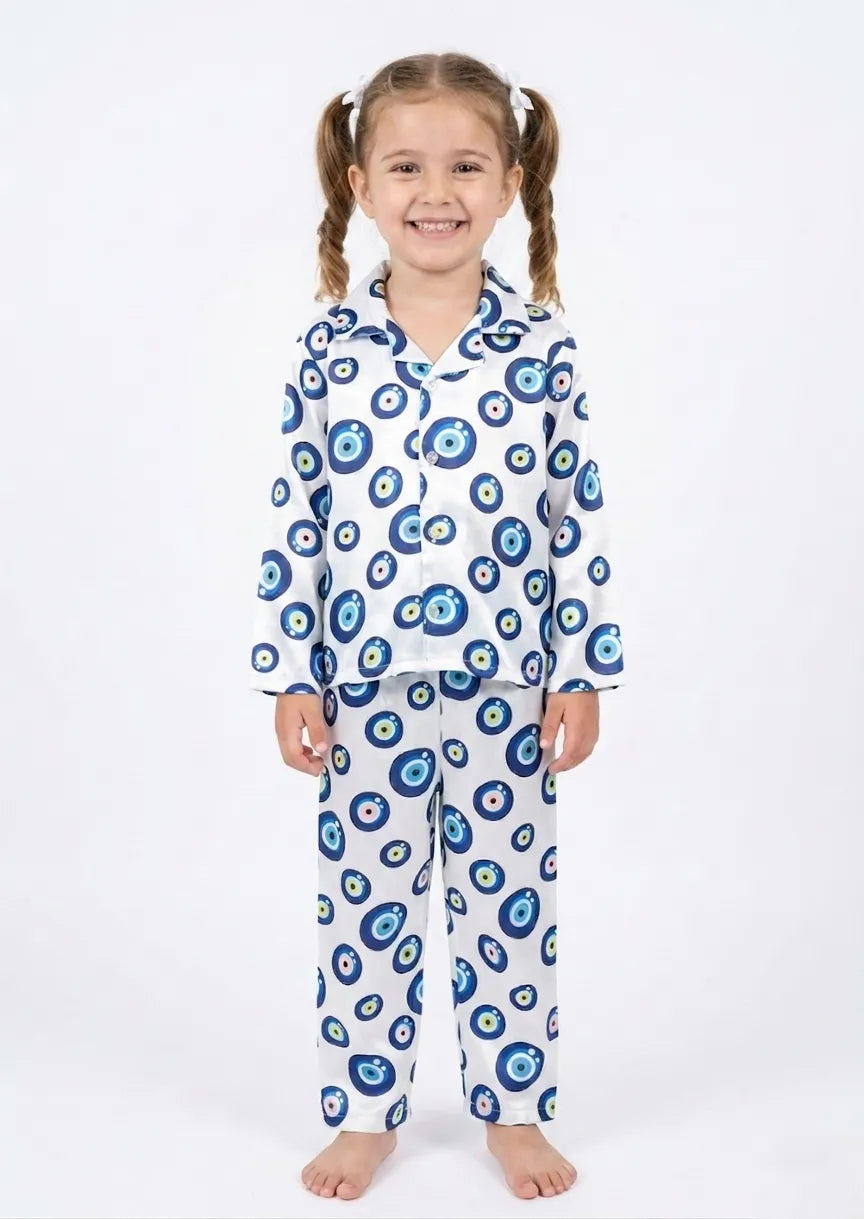 A young girl smiling while wearing a white satin night suit with a blue evil eye print.
