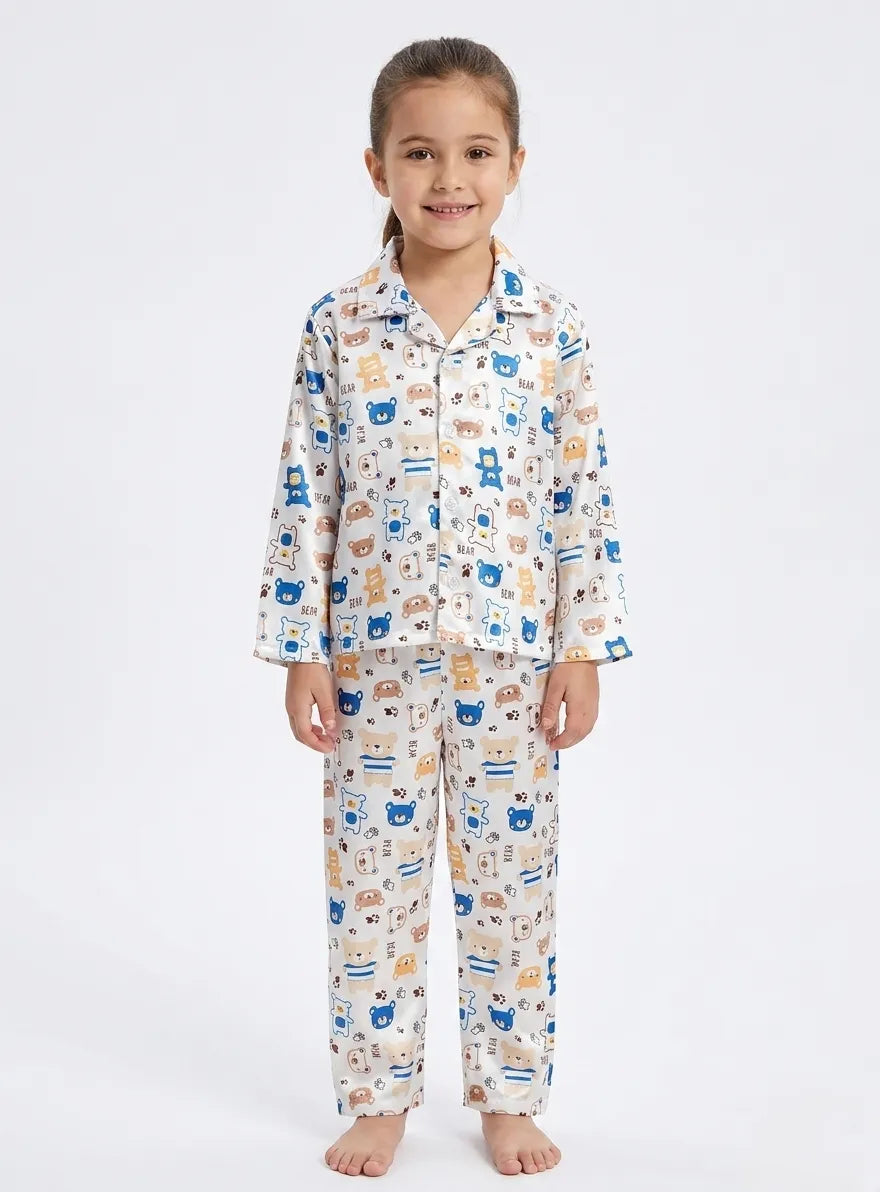 A young girl sitting cross-legged wearing a white satin night suit with a blue and brown bear print.
