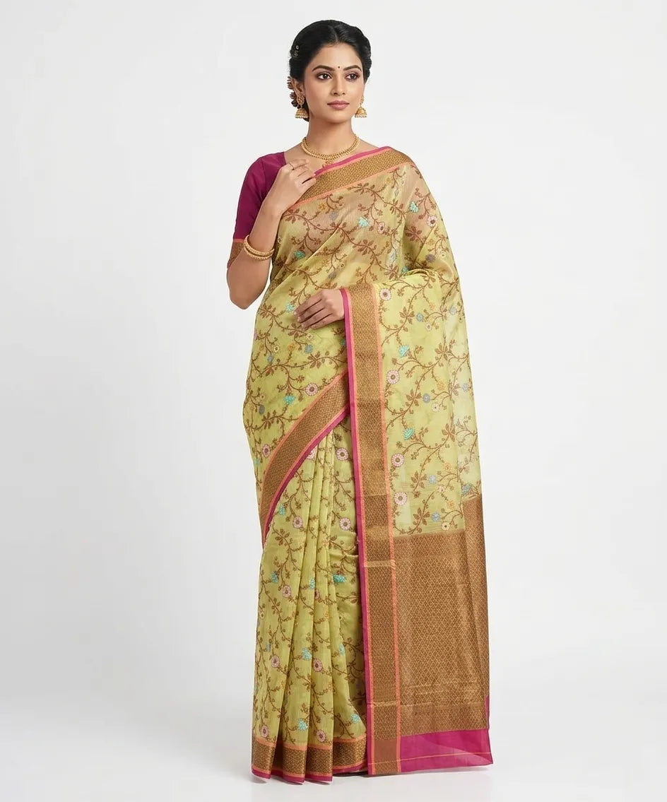 An Indian woman modeling an olive green silk blend saree with a floral vine woven pattern, featuring a bronze zari border and magenta piping. She wears a magenta blouse and gold jewelry against a plain white background.
