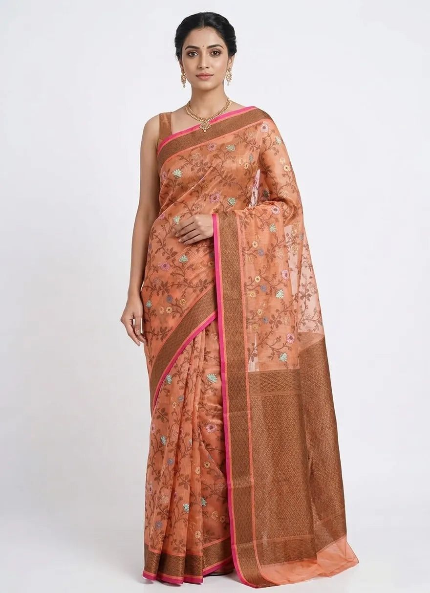Woman in a rust orange floral organza saree featuring a bronze zari border and pink piping.
