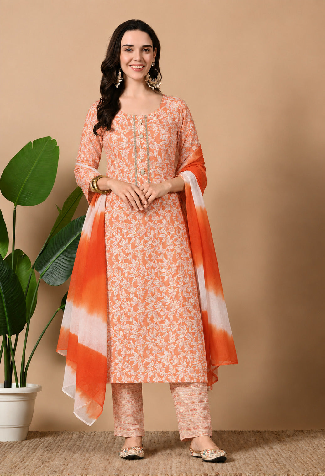 Orange printed ethnic suit set featuring intricate white floral patterns on the kurta, matching printed straight trousers, and a coordinating orange and white dupatta. Designed with a round neckline, three-quarter sleeves, and an elegant straight silhouette, perfect for festive occasions, casual outings, and everyday ethnic wear.