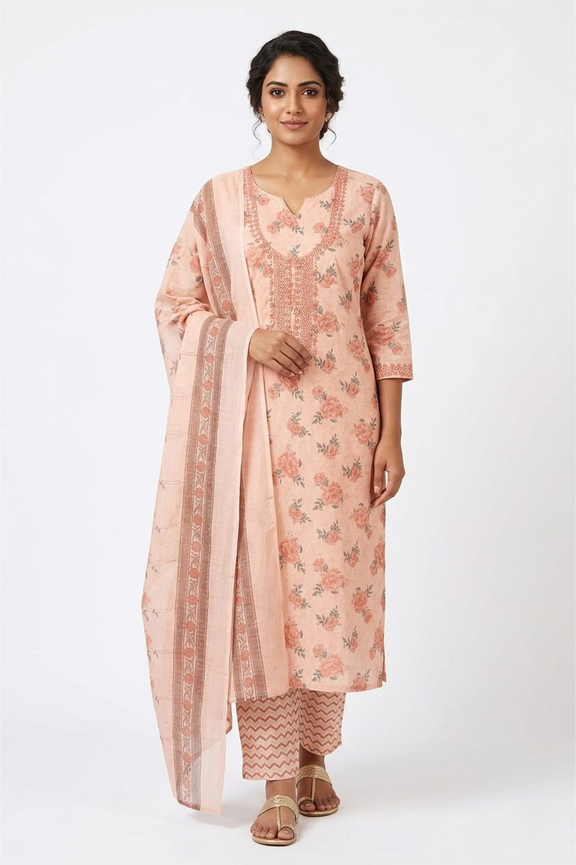 A soft peach cotton unstitched suit with red floral prints and a sequin-embroidered neckline, paired with a matching dupatta and chevron-print bottom.
