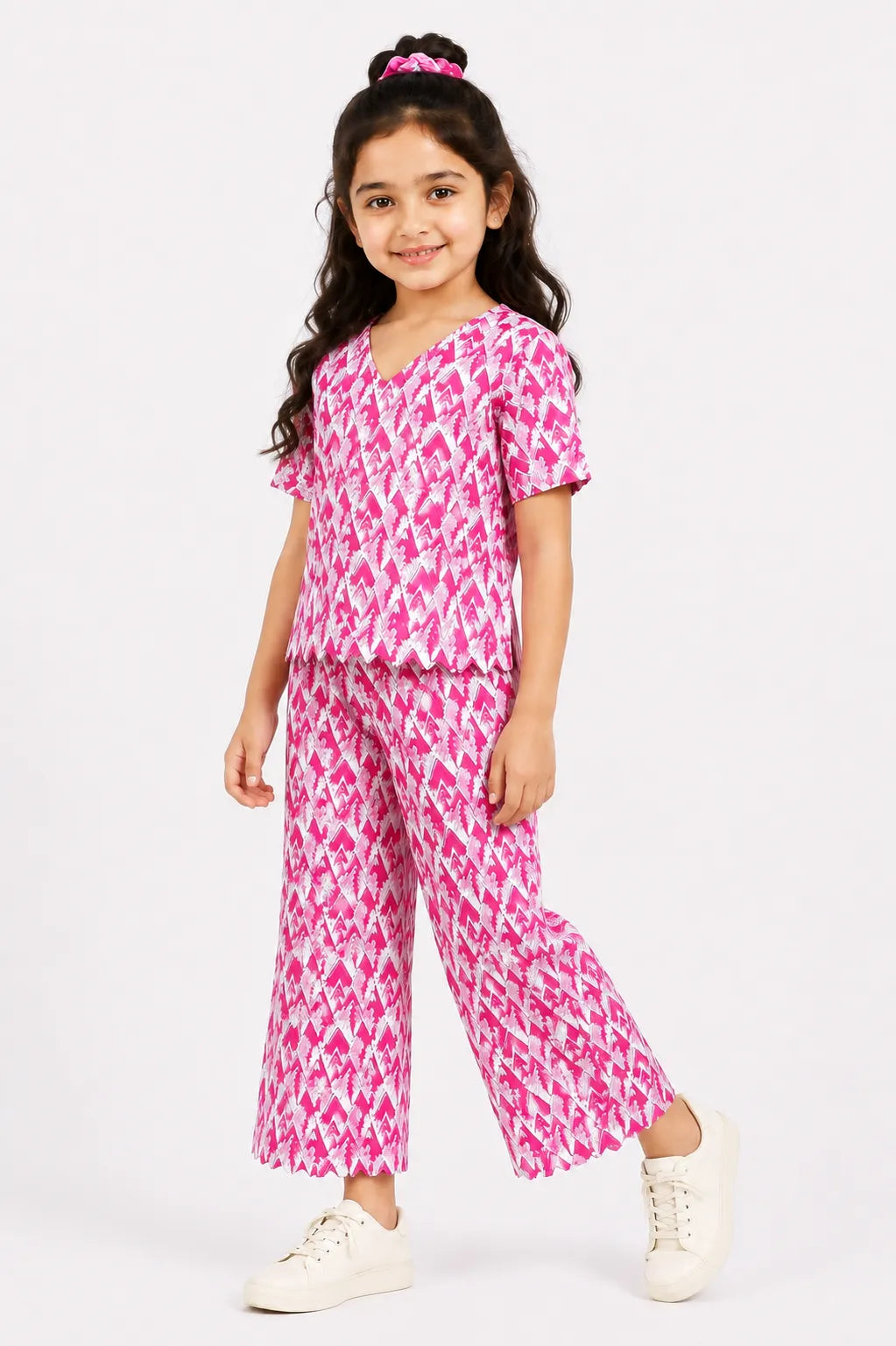 Young girl posing in a pink and white ikat geometric printed co-ord set with a V-neck scallop-hem top and wide-leg trousers.
