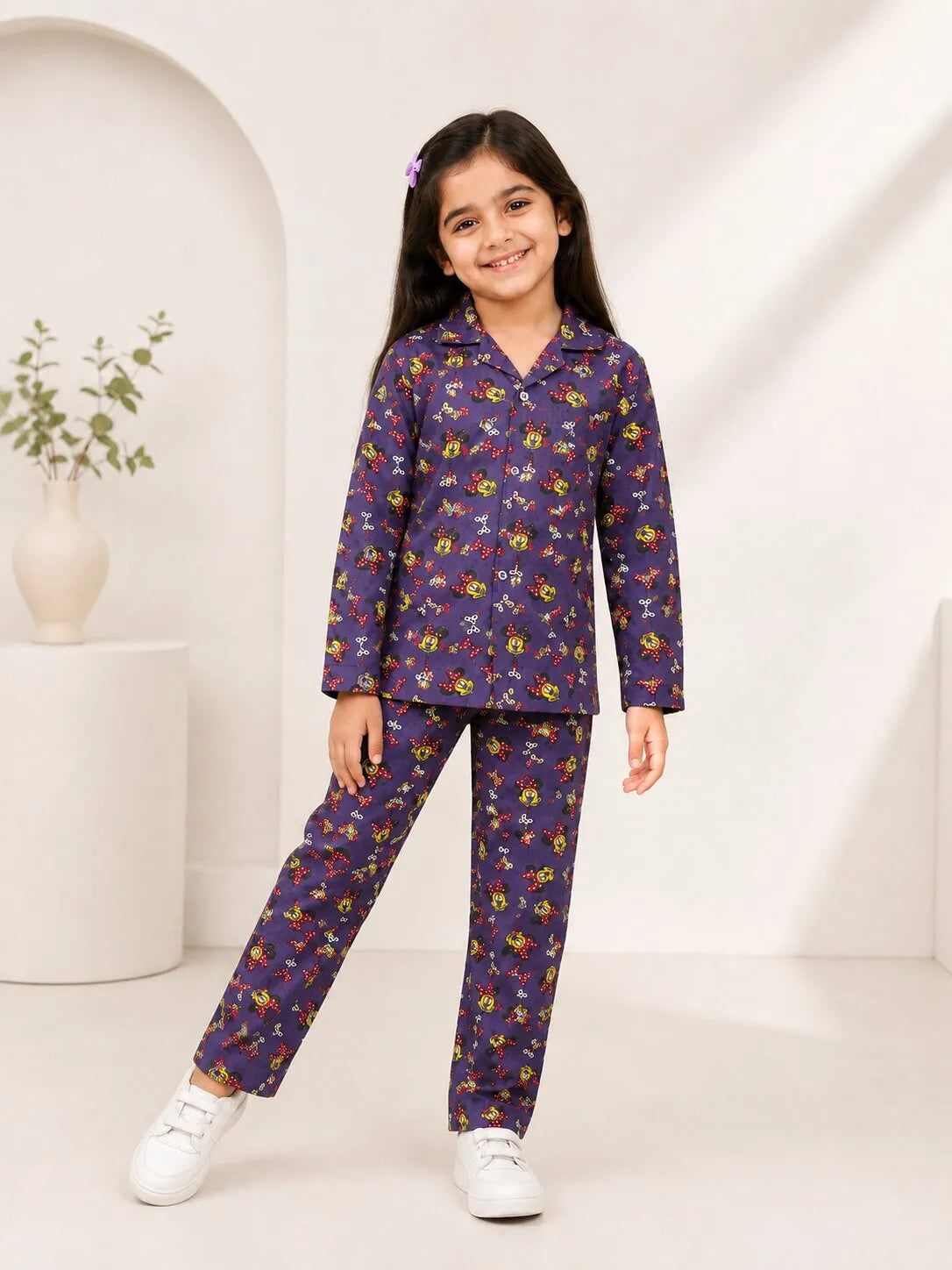 A young girl smiling while wearing a mauve purple cotton night suit with a cartoon character and bow print.