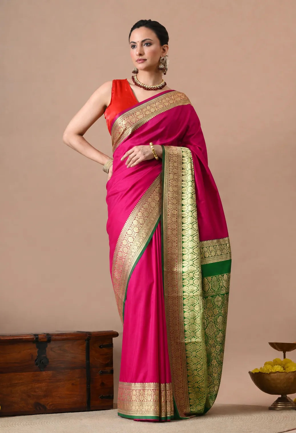 Woman wearing a rani pink silk saree with gold zari borders and a green pallu.