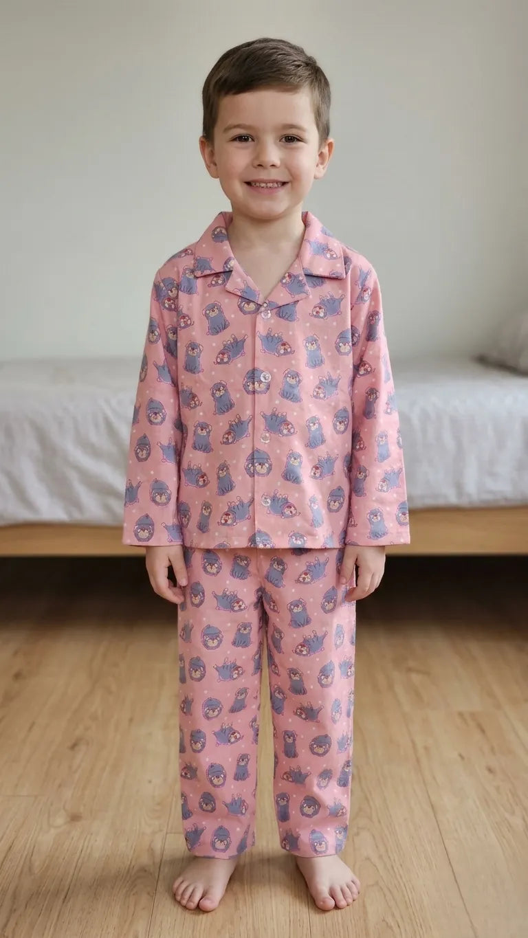 Young boy in a pink cotton night suit with grey pug dog prints, featuring a button-up notched collar shirt and matching pyjamas.
