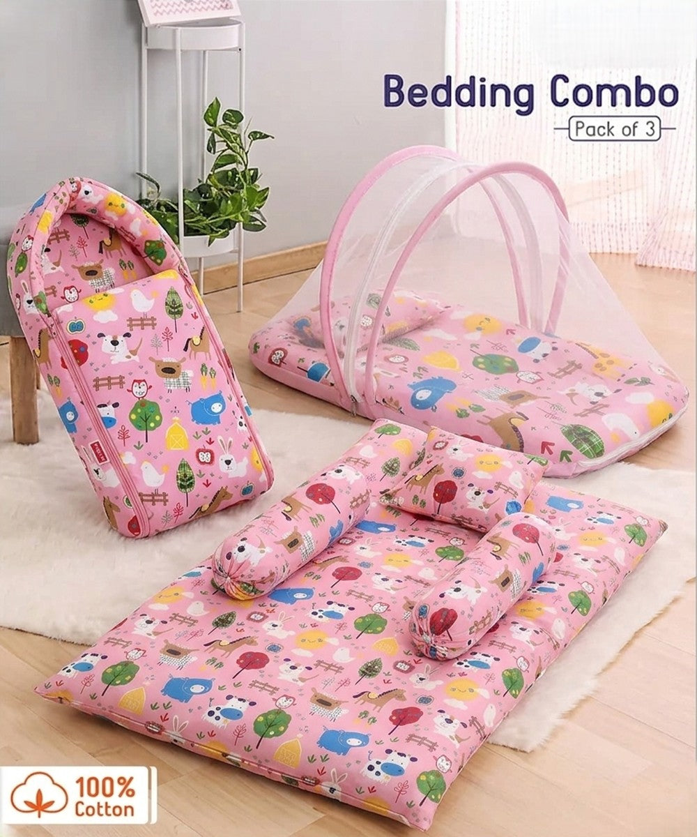 Pink and white printed 3-in-1 infant bedding combo featuring a zip-up carry nest, a mattress with an attached mosquito net, and a matching pillow with bolsters on a wooden floor.