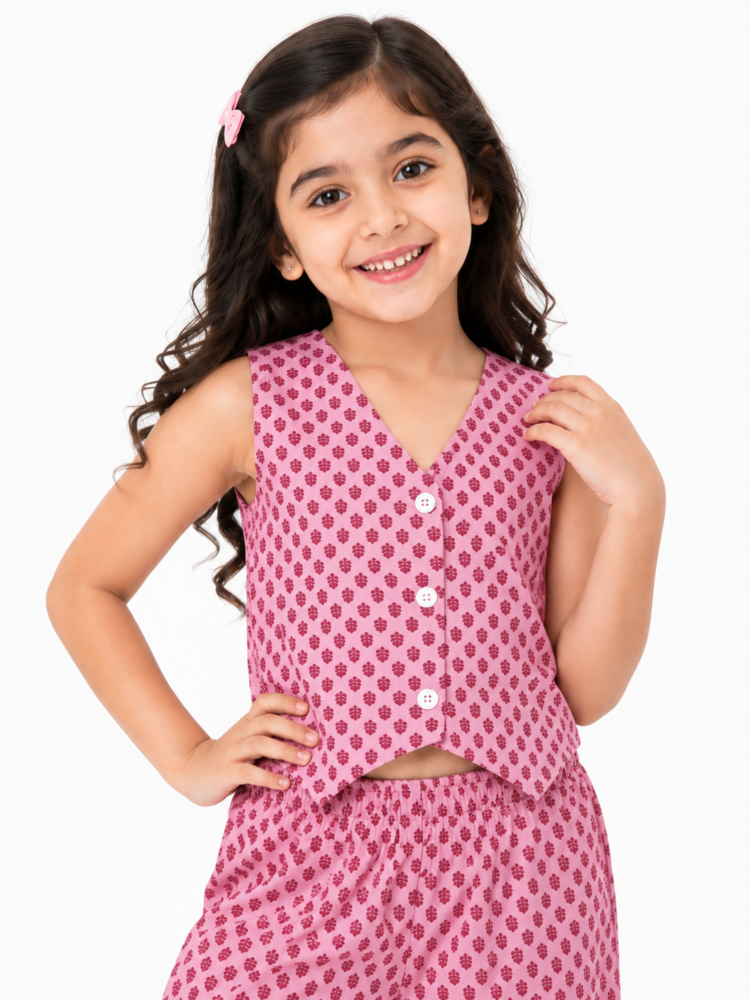 A young girl smiling in a pink pure cotton co-ord set featuring a tiny dark pink motif print, consisting of a sleeveless button-down vest top and relaxed wide-leg trousers
