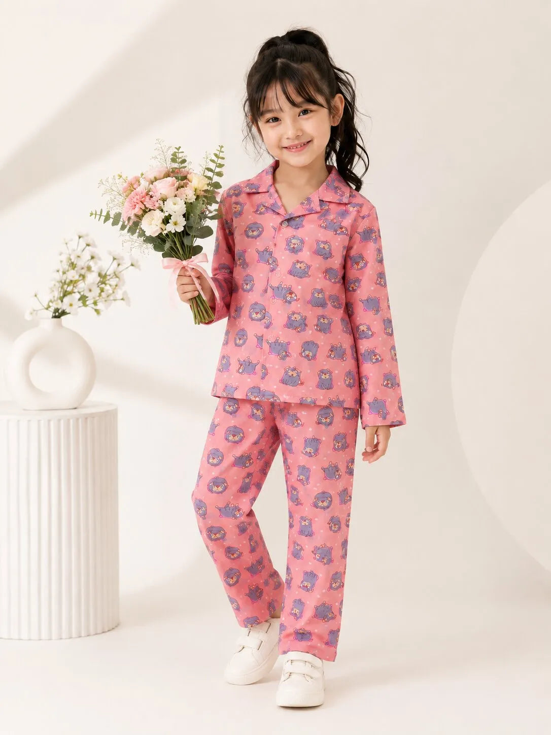 A child standing in a bedroom wearing a pink cotton night suit with a purple puppy and white polka dot print.