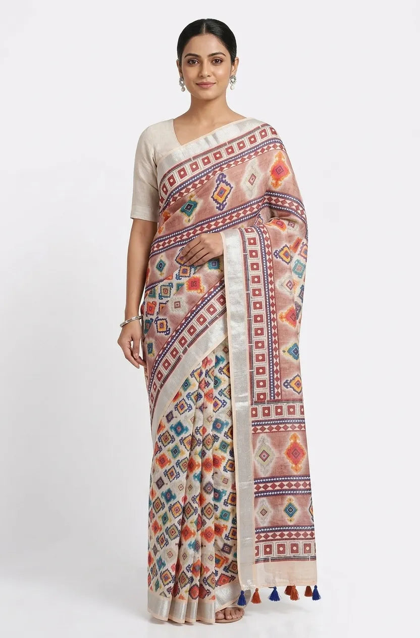 A woman wearing a beige and mauve cotton saree with multi-colored geometric diamond prints, a silver zari border, and blue tassels at the end.