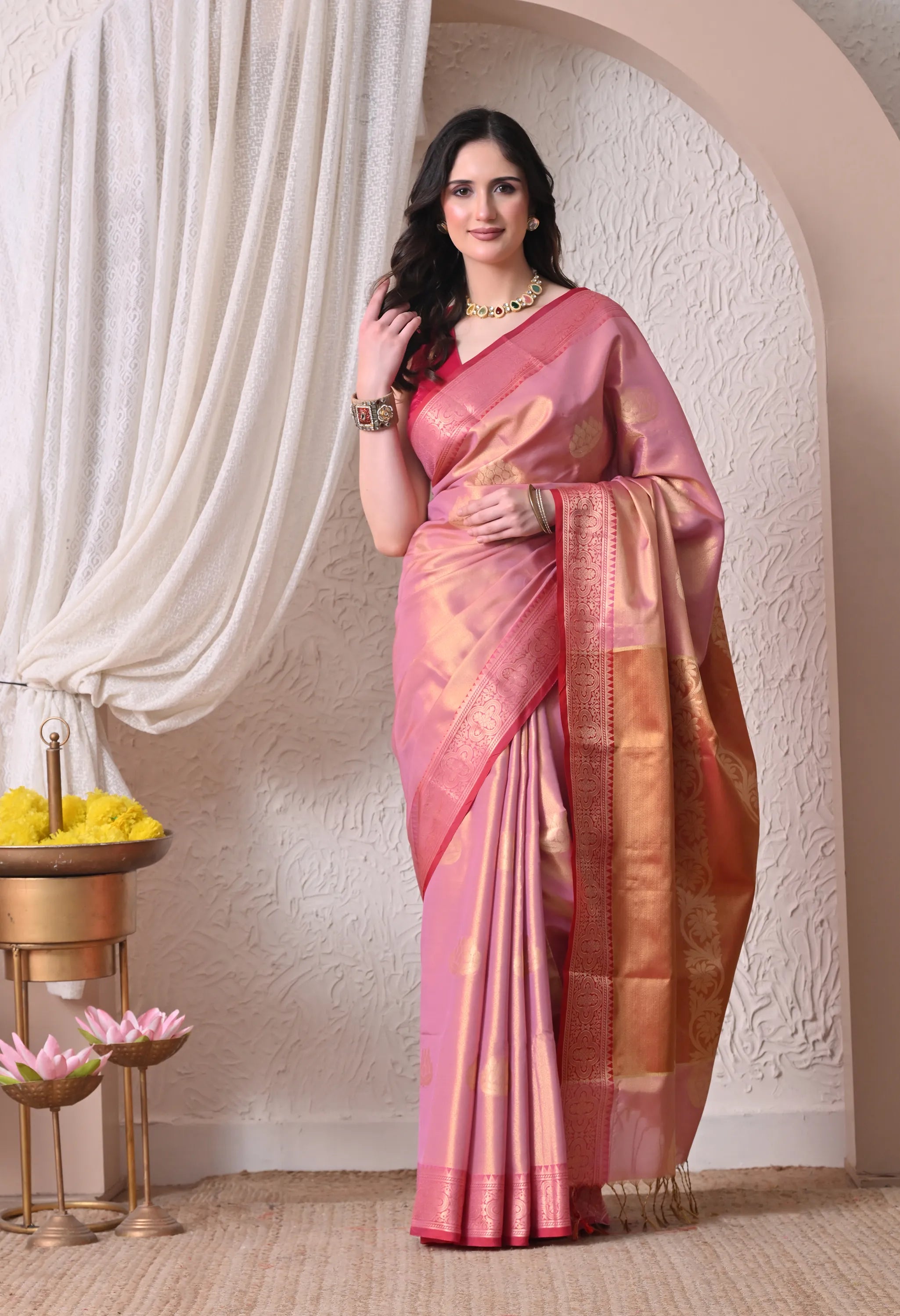 An elegant pink silk blend saree with a luminous sheen, decorated with large golden zari motifs, an opulent golden border, and a rich, traditional pallu.
