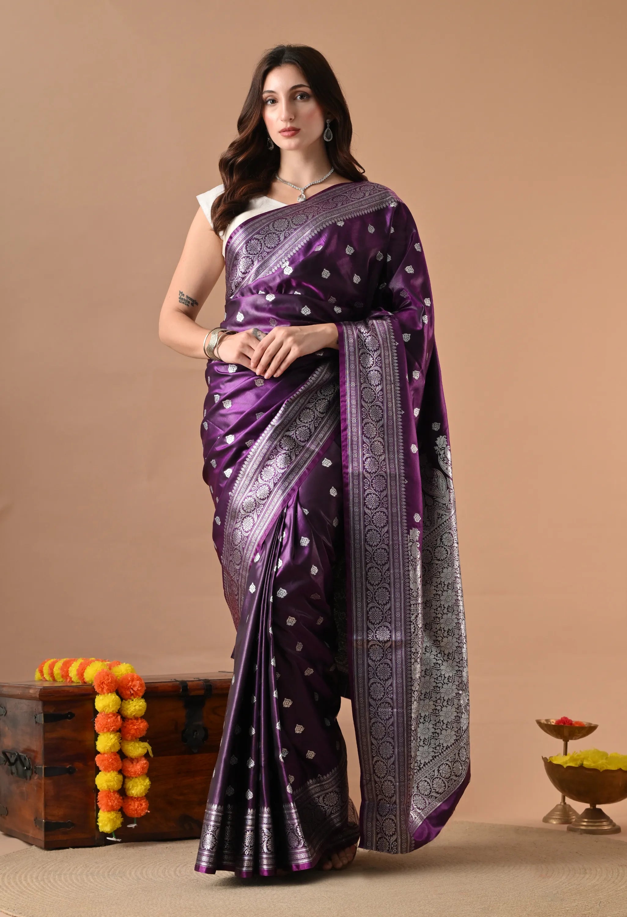 A woman in a vibrant purple silk blend saree with intricate silver woven floral patterns and a wide ornamental border.