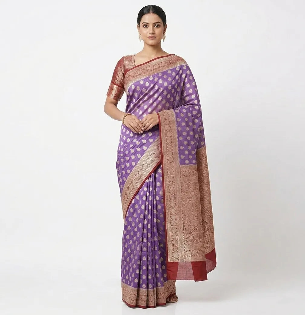 A woman posing in a rich purple Banarasi silk blend saree featuring gold-toned woven motifs and a thick gold-maroon zari border, paired with a maroon elbow-length sleeve blouse.
