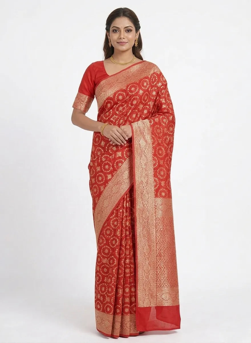 A woman posing in a rich red Banarasi saree featuring gold-toned circular woven motifs (Butis) spread across the body and a broad, ornate zari border.