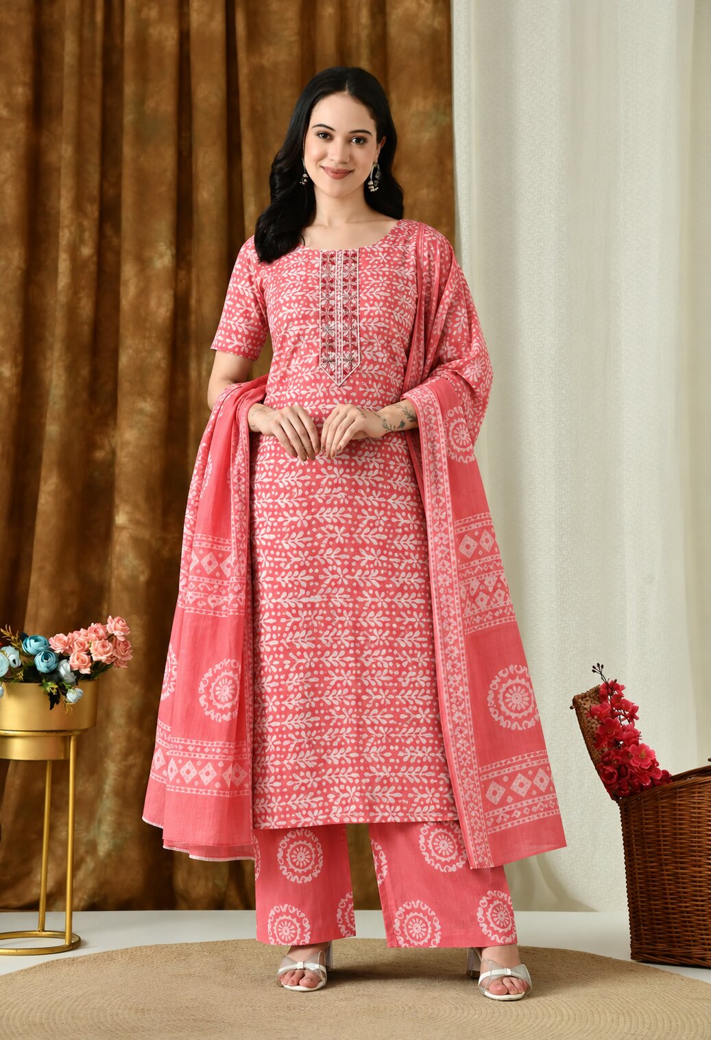 Coral pink ethnic kurta suit with white floral and geometric prints, square neckline with decorative detailing, matching printed palazzo pants, and a coordinating dupatta featuring traditional white motifs and a patterned border.