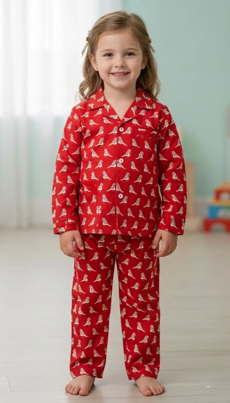 A young girl smiling while wearing a red long-sleeved pajama set featuring a white all-over bird motif, standing against a dark background