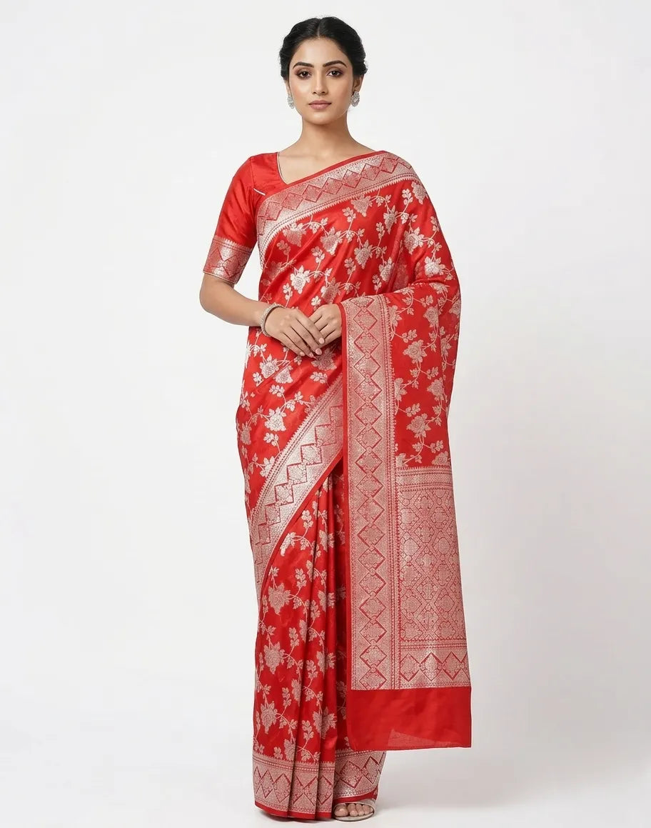 A woman modeling a bright red silk-blend saree featuring silver floral rose patterns and a wide zari border, styled with a matching red blouse against a white background.
