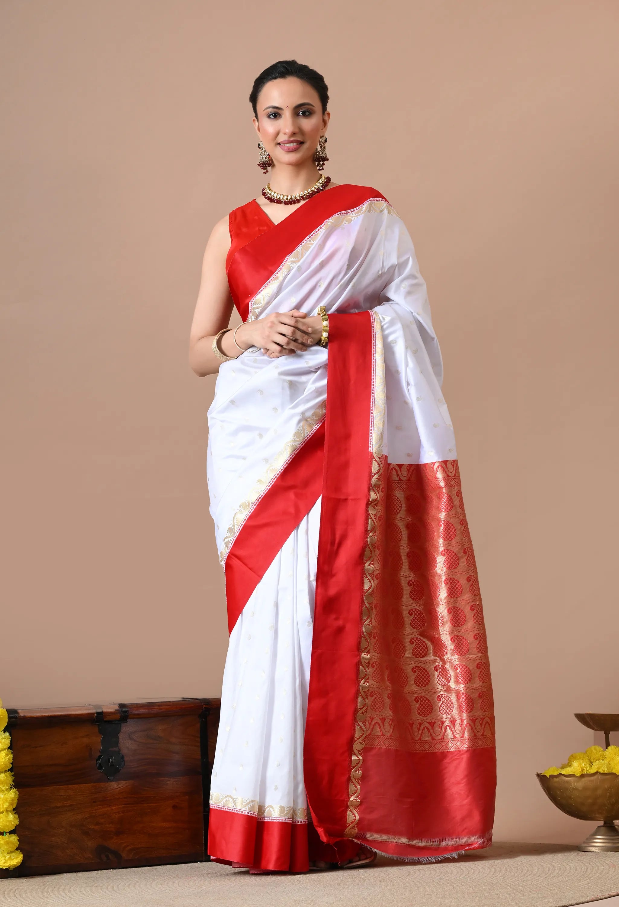 Woman posing in a white and red Banarasi silk blend saree with intricate gold zari woven borders and floral motifs on the pallu.