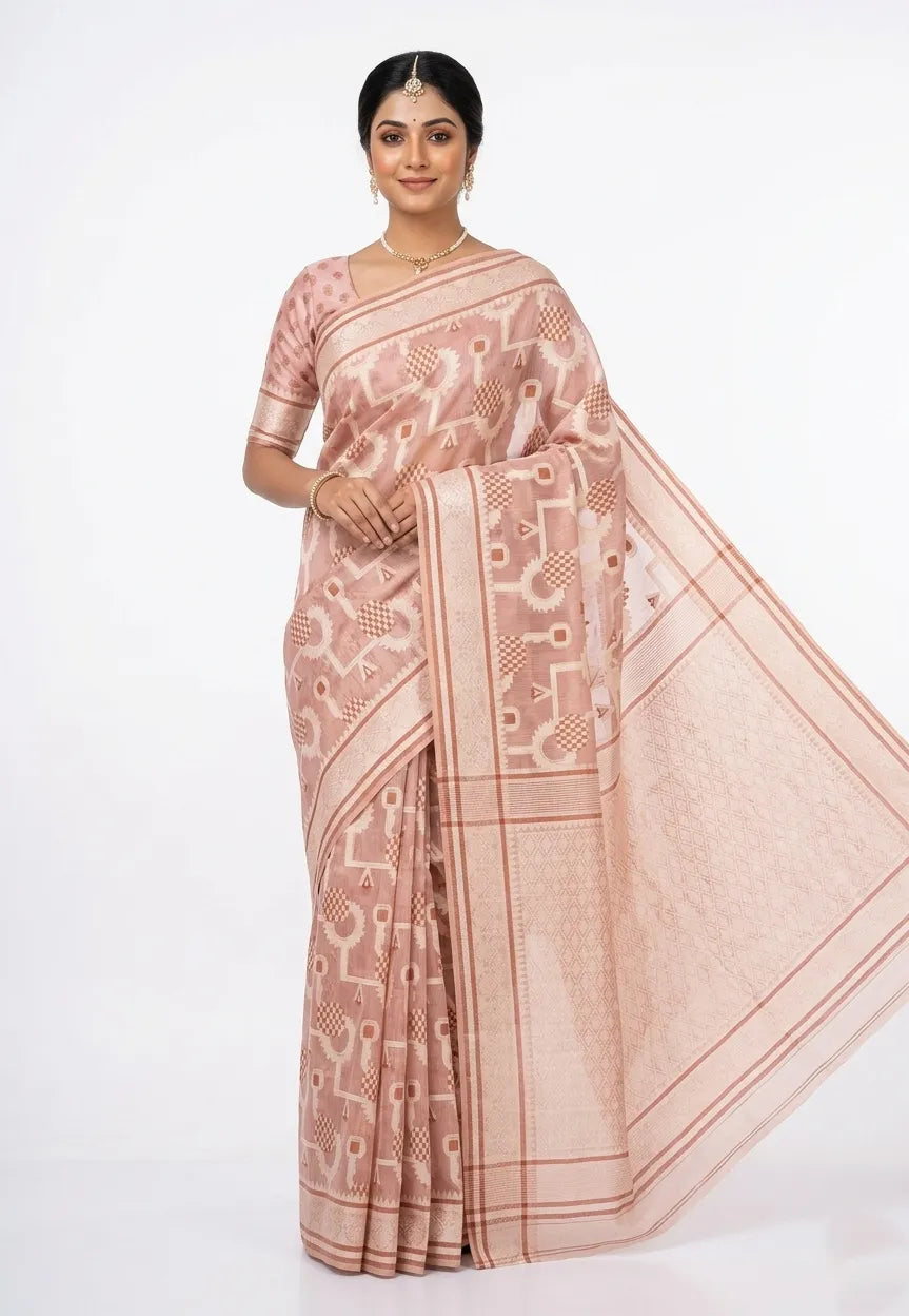 A woman posing in a rose-gold-colored silk blend saree featuring intricate geometric white and gold woven patterns. She is wearing a matching half-sleeved blouse, a traditional gold maang tikka, necklace, and earrings. The saree has a wide decorative zari border and a detailed pallu, set against a plain white background.
