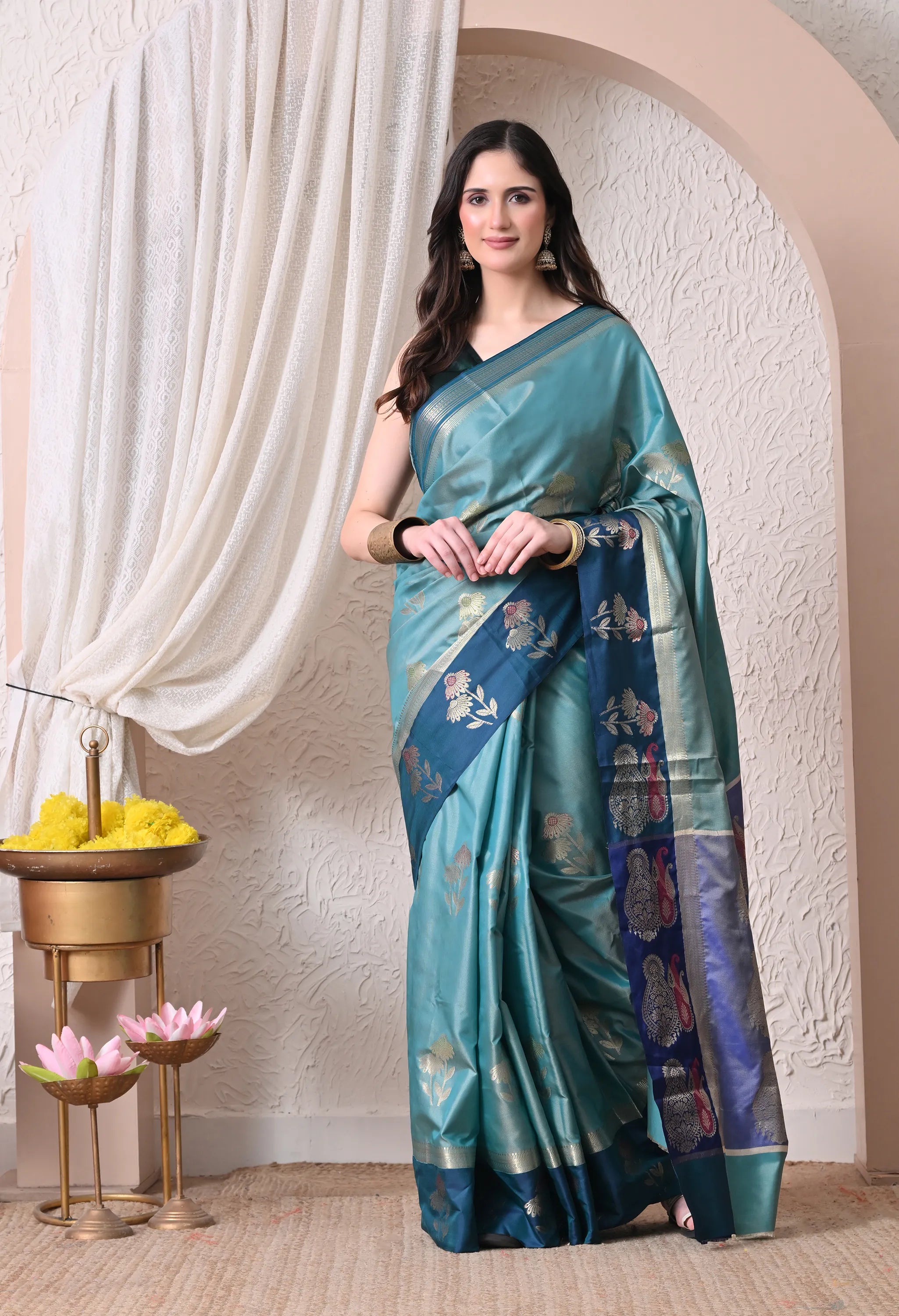 A woman modeling a sea green silk blend saree featuring a contrasting deep peacock blue border and pallu intricately woven with golden and silver zari floral motifs.
