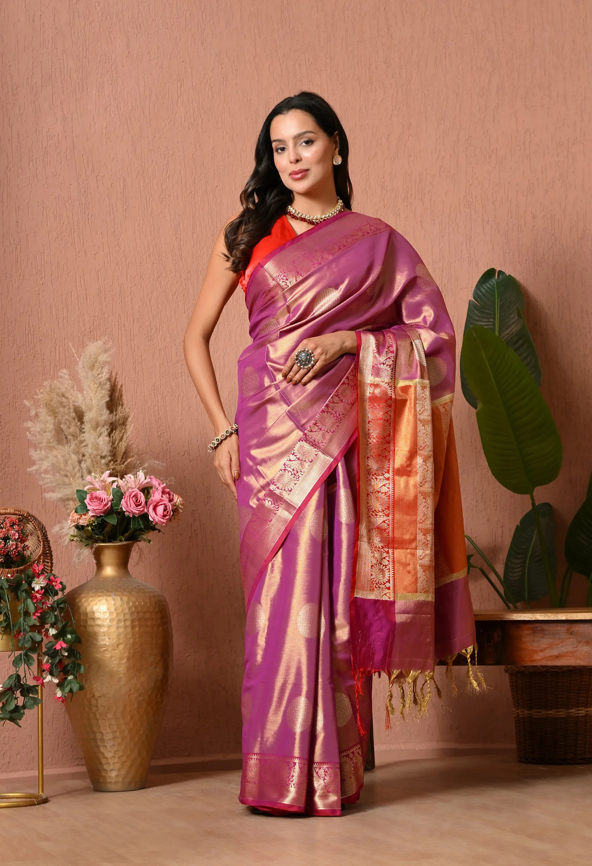A woman posing beautifully in an orchid mauve silk blend saree featuring large circular gold motifs and a contrasting multi-colored orange and gold zari pallu.
