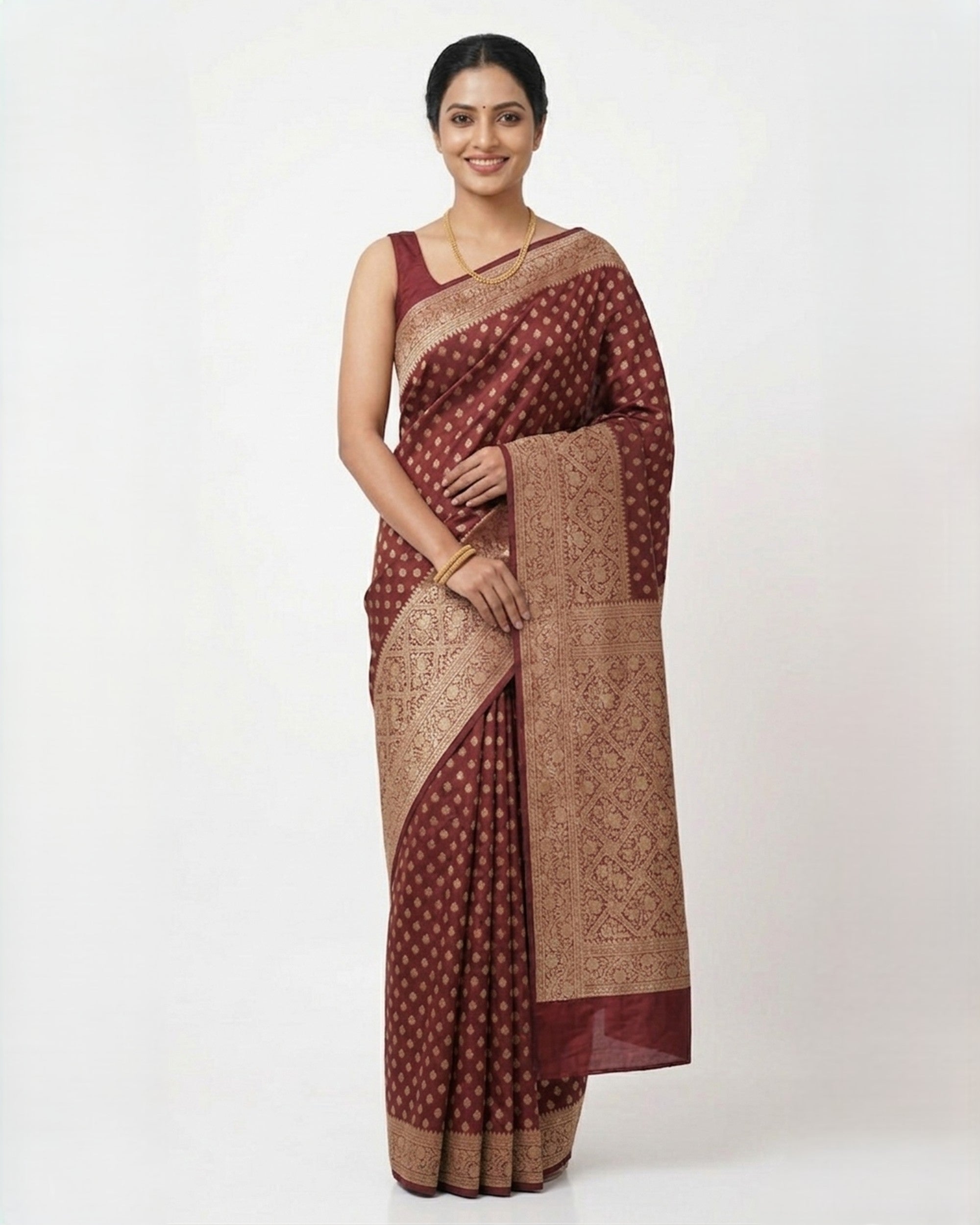 A woman wearing a deep maroon Banarasi silk saree featuring a dense gold zari grid pattern and a broad, intricate gold border, paired with a matching sleeveless maroon blouse against a white background.