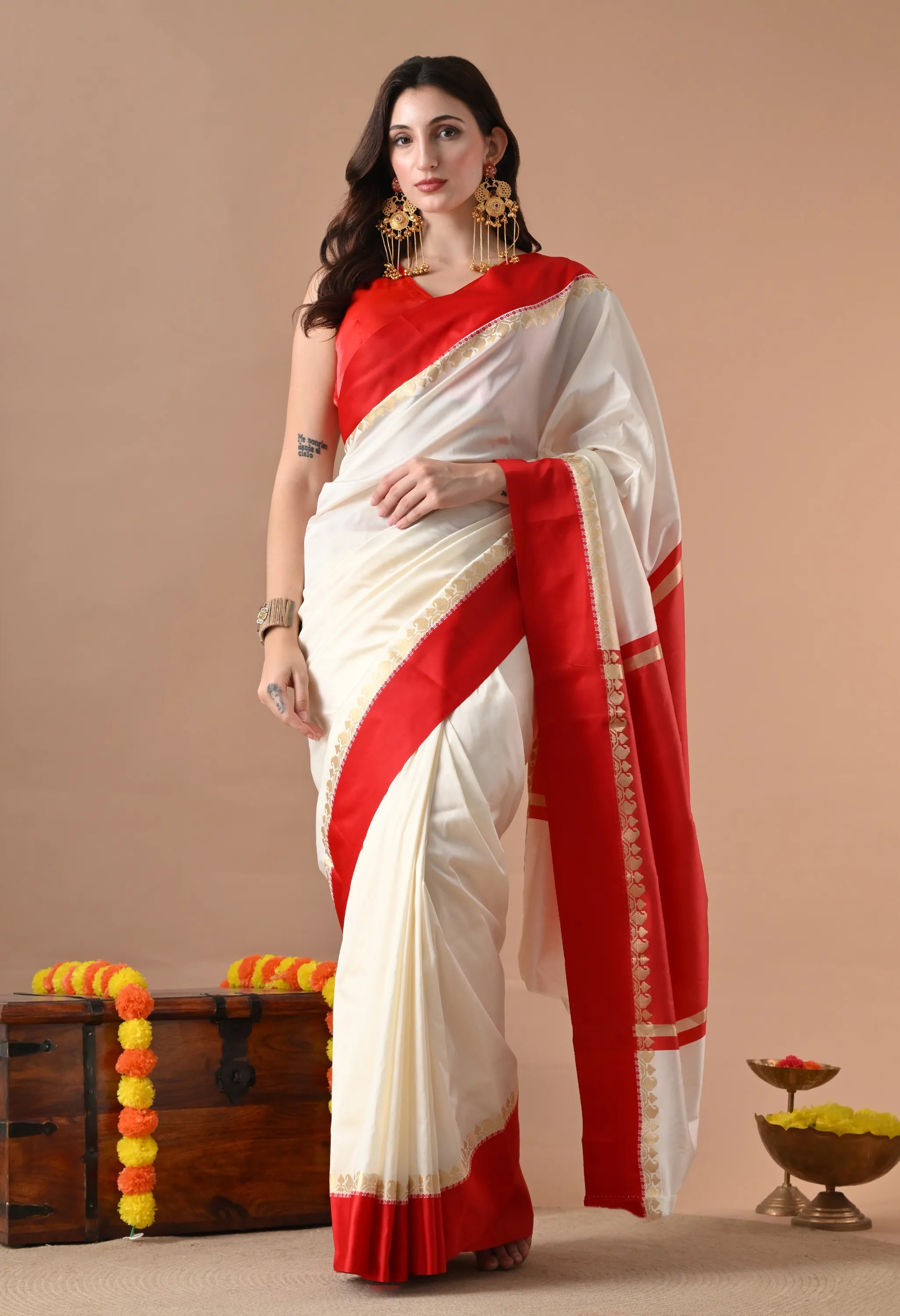 Woman posing in an ivory silk blend saree with a wide red zari border and matching red sleeveless blouse.