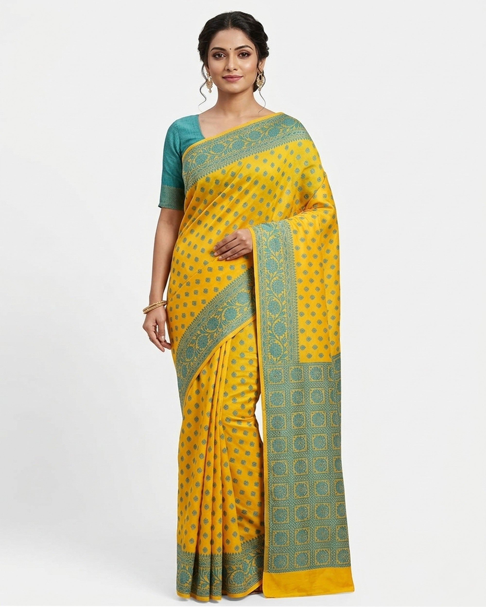 A smiling woman posing in a vibrant yellow saree featuring an intricate green patterned border and a teal green blouse against a plain white background.