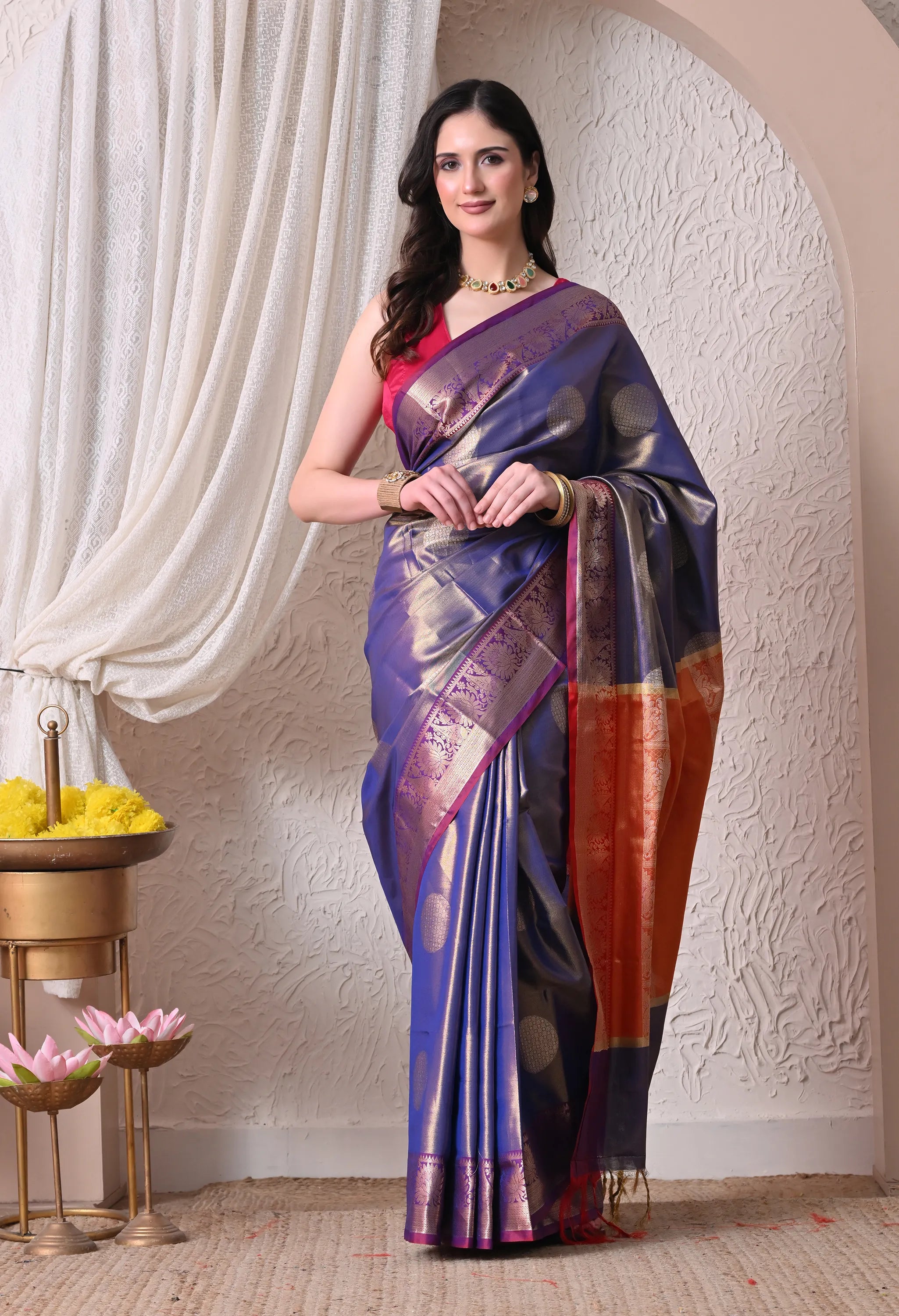 A regal royal blue silk blend saree featuring large circular golden zari motifs, a detailed borders, and a striking rust-orange contrast block on the tassel-tipped pallu.
