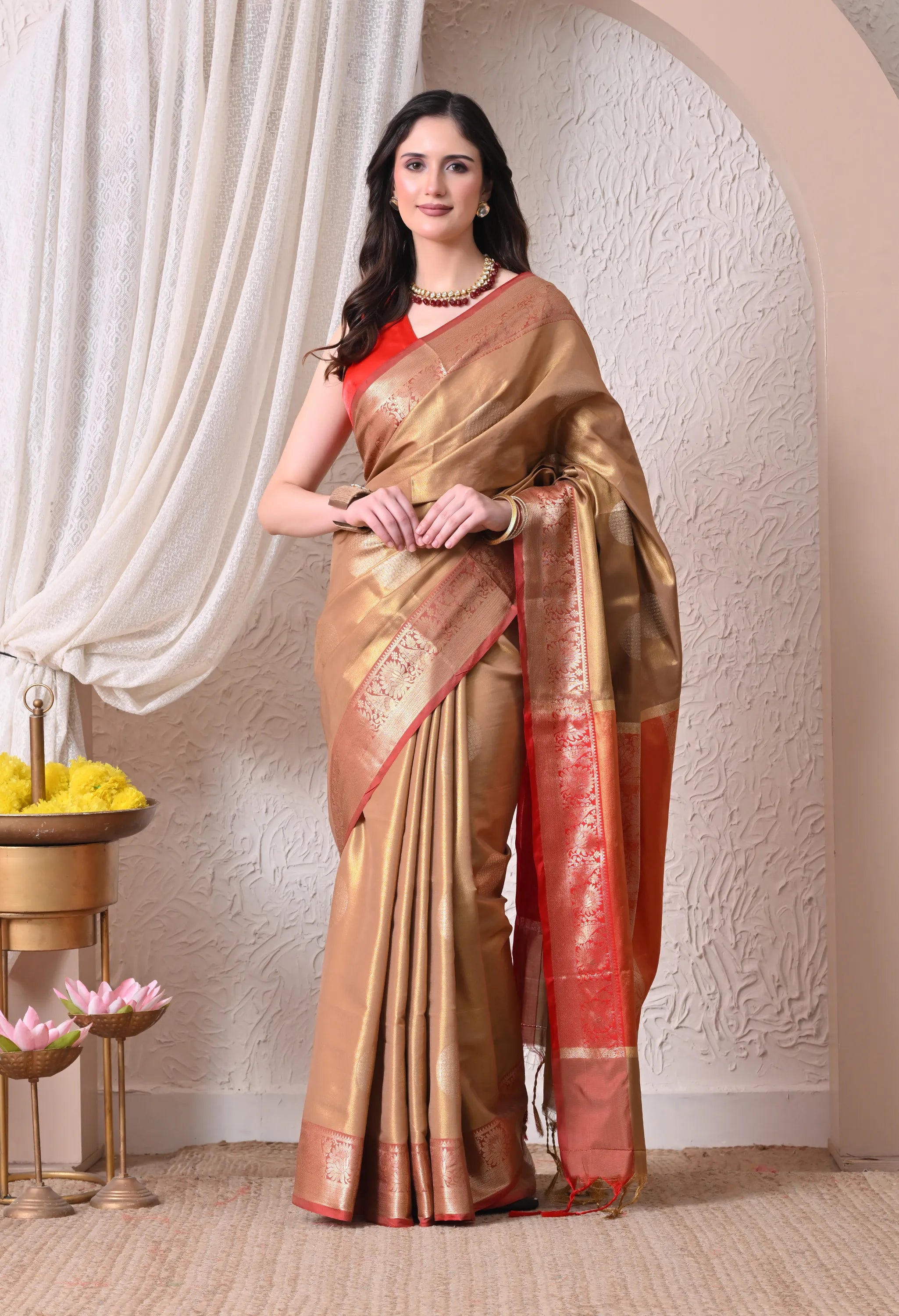 A woman elegantly carrying an antique gold silk blend saree featuring subtle circular motifs and a contrasting crimson red zari border and pallu.
