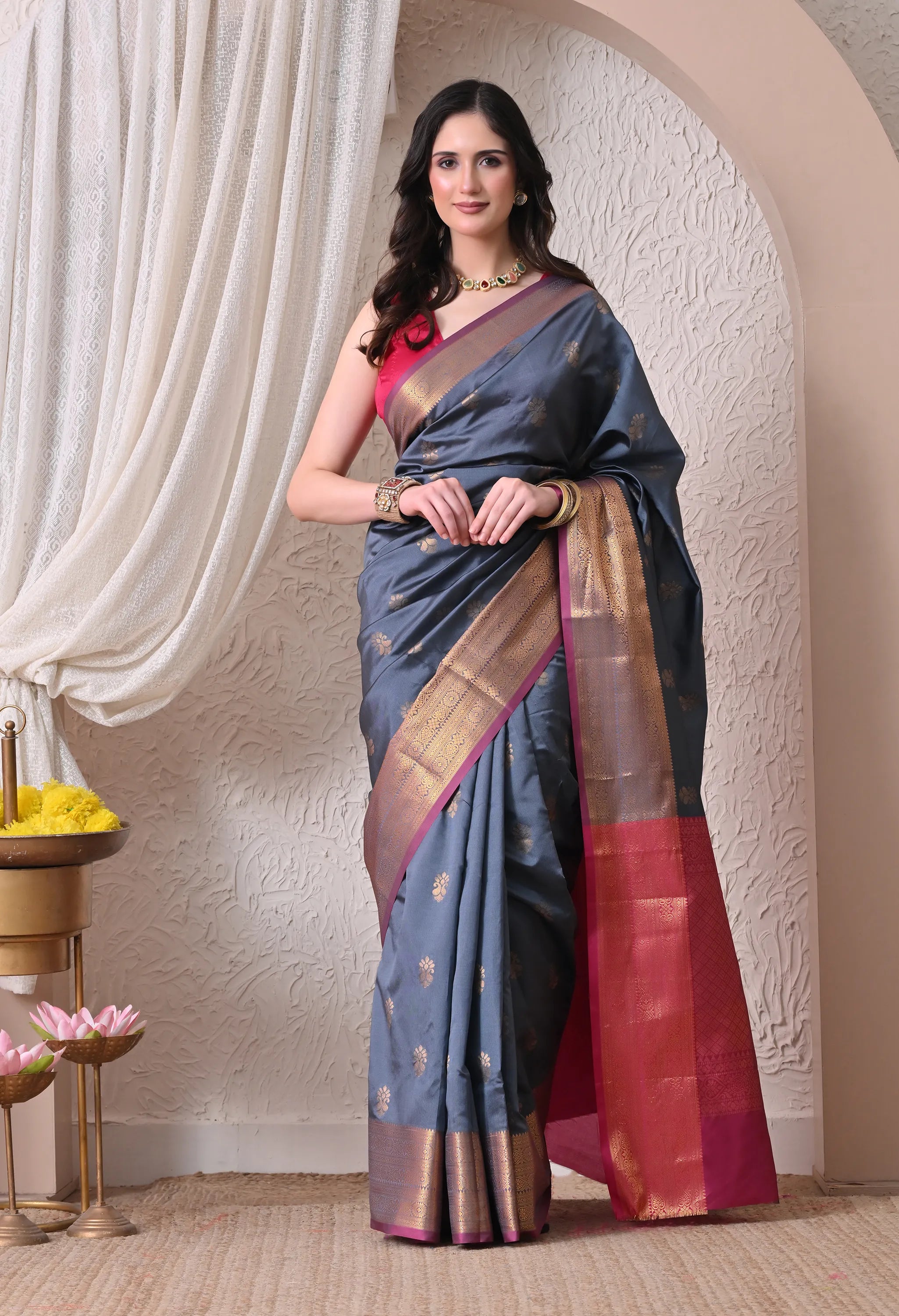 A woman modeling a steel grey silk blend saree with small gold floral motifs, featuring a striking contrast magenta pink and intricately woven gold zari border and pallu.
