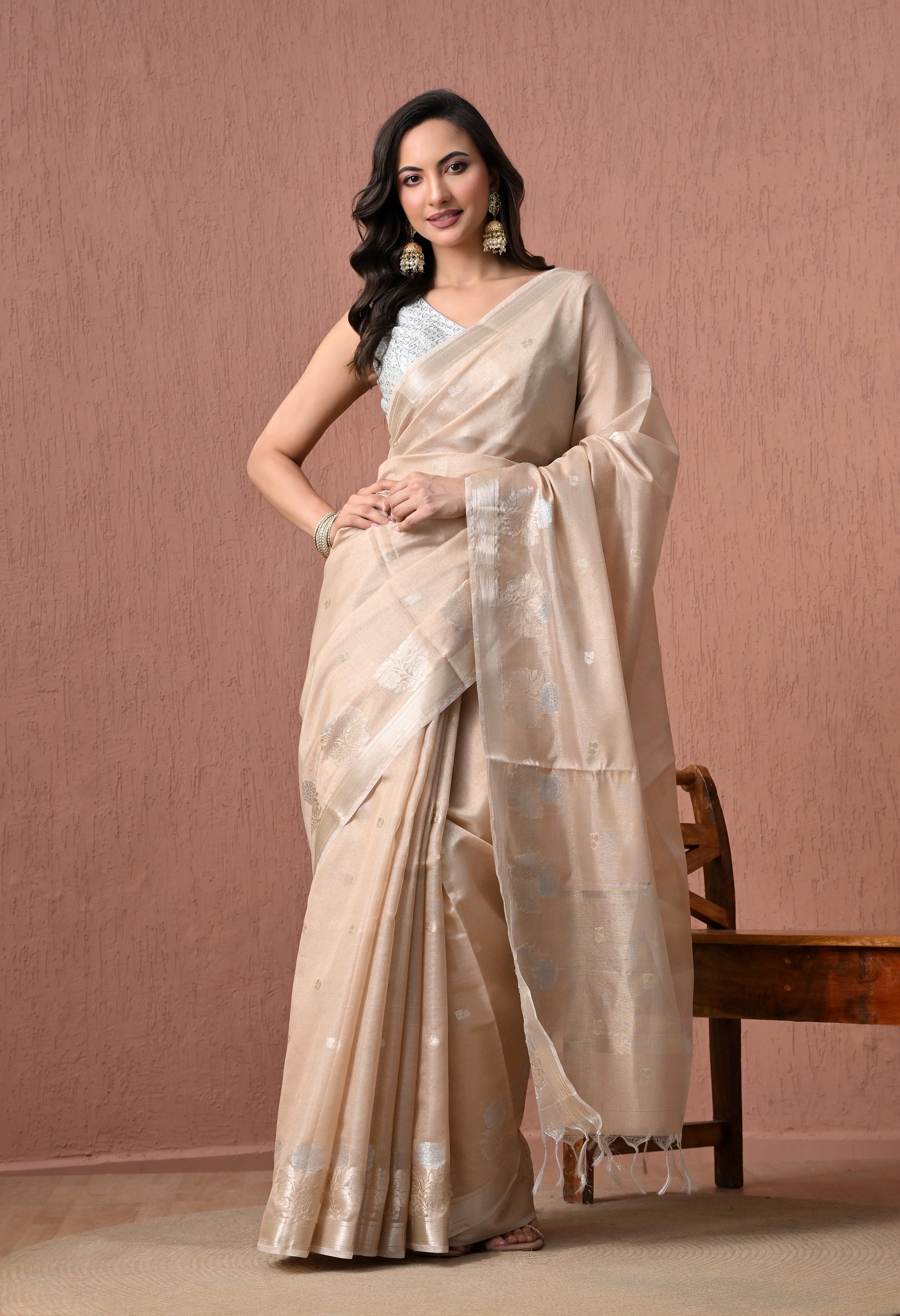 A woman poses in an elegant off-white pure cotton handloom saree featuring fine silver zari floral motifs and a tasseled pallu, paired with a silver-grey sleeveless embroidered blouse.
