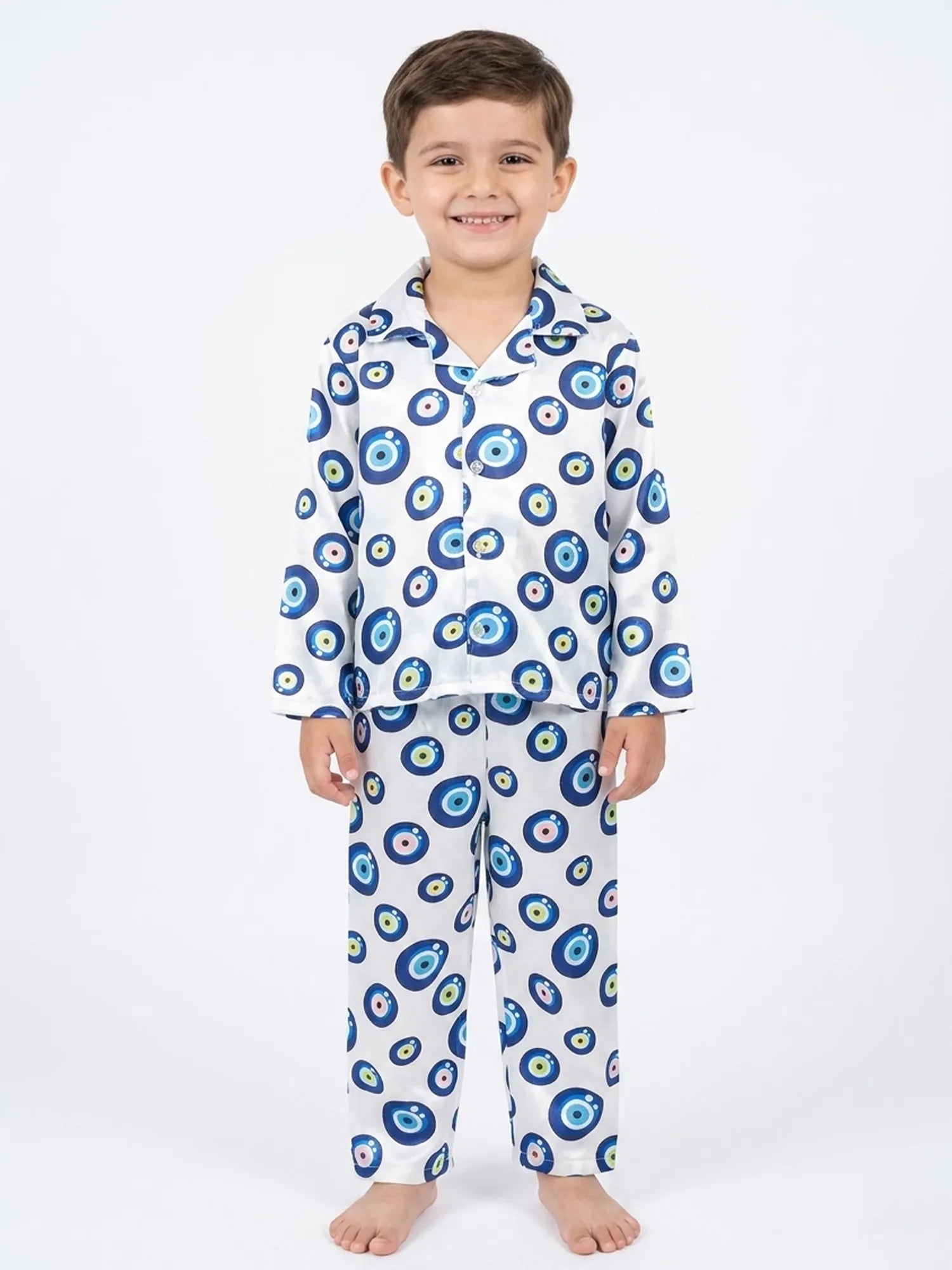 A young boy smiling while wearing a white satin night suit with a blue evil eye print.
