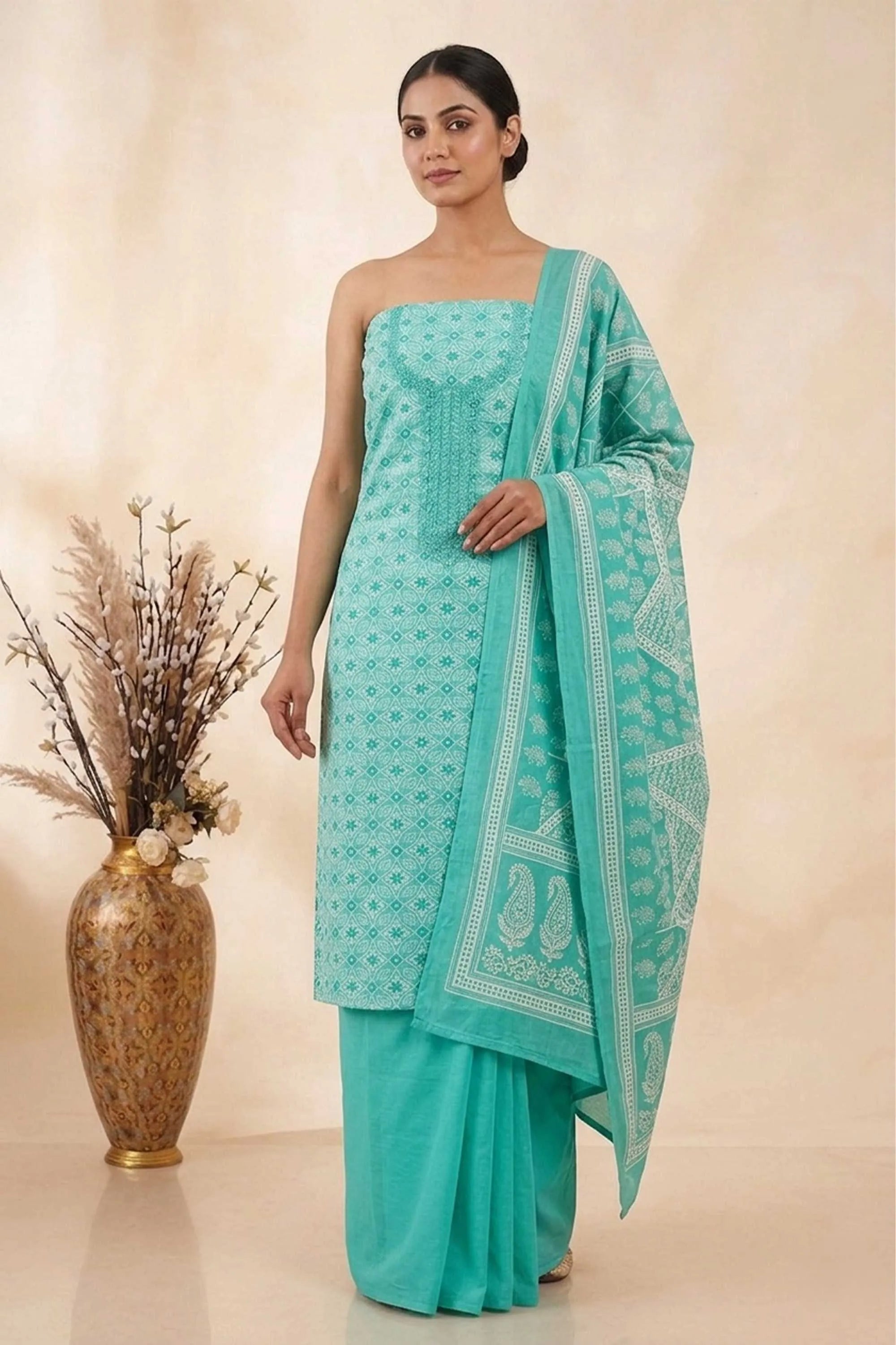 A woman posing in a beautiful sea green unstitched ethnic suit set. The outfit features a patterned straight kurta, a matching dupatta with traditional motifs, and a solid sea green bottom.