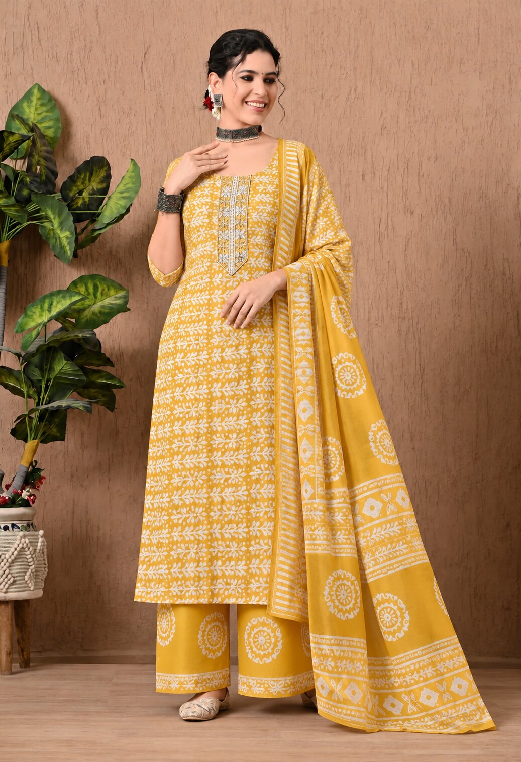 Mustard yellow ethnic kurta suit with white floral prints, intricate embroidery around the neckline, matching printed palazzo pants, and a coordinating dupatta featuring traditional white motifs and a decorative border.
