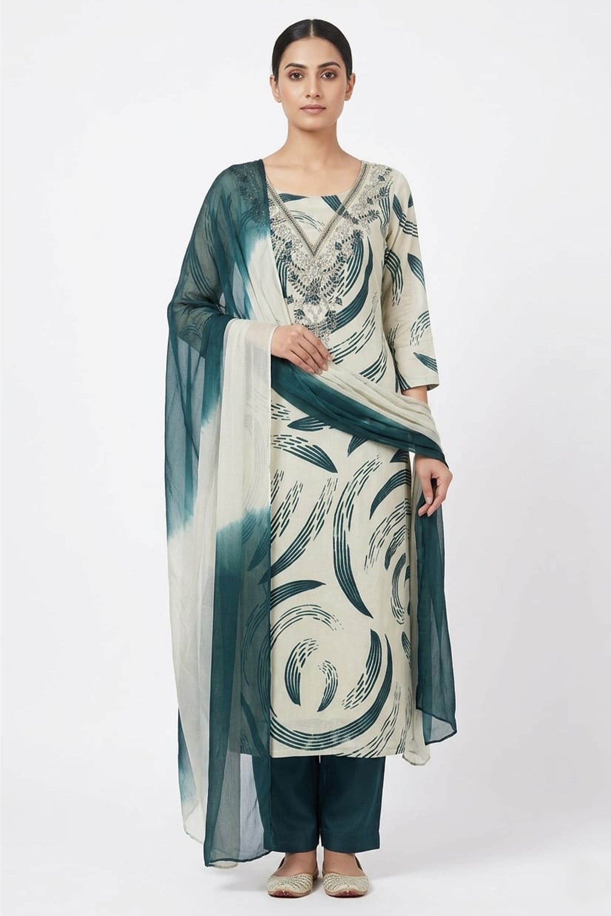 An off-white cotton unstitched suit with bold sea green abstract swirls and a silver embroidered V-neckline, draped with a shaded ombré dupatta.
