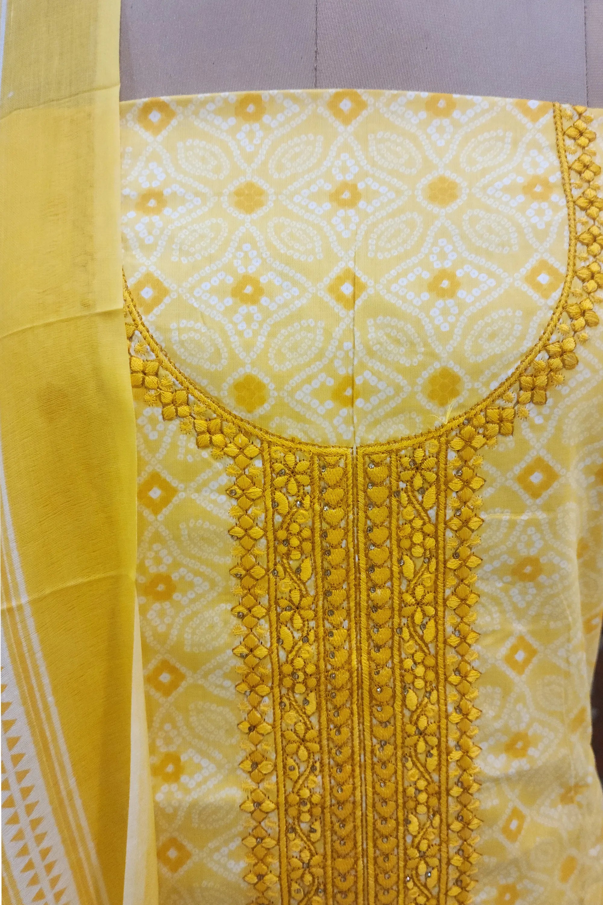 Yellow Bandhani print unstitched suit with heavy neck embroidery and matching dupatta, traditional Indian ethnic wear for women.