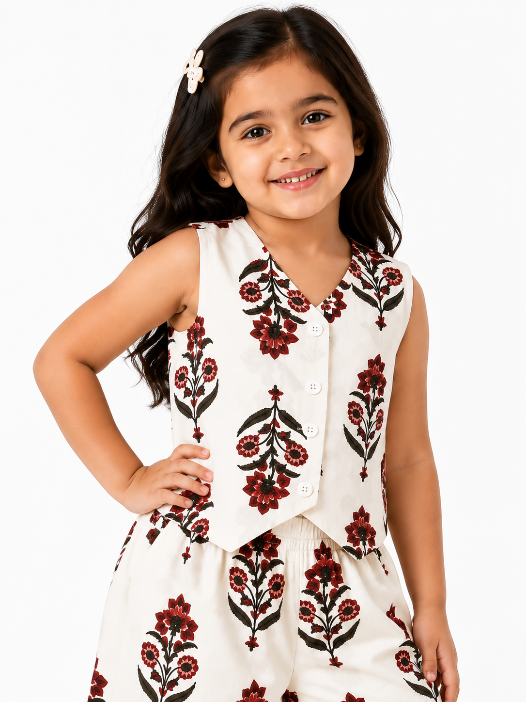 A young girl smiling while wearing an off-white pure cotton co-ord set featuring a sleeveless waistcoat top and wide-leg trousers adorned with a maroon and green floral boota print

