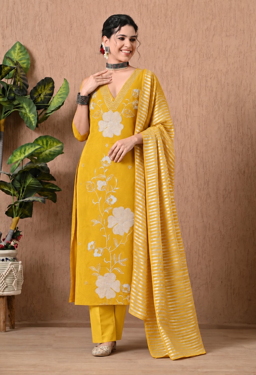 Mustard yellow women’s ethnic suit set featuring a straight kurta with white floral embroidery, matching trousers, and a striped dupatta with an elegant traditional design.

