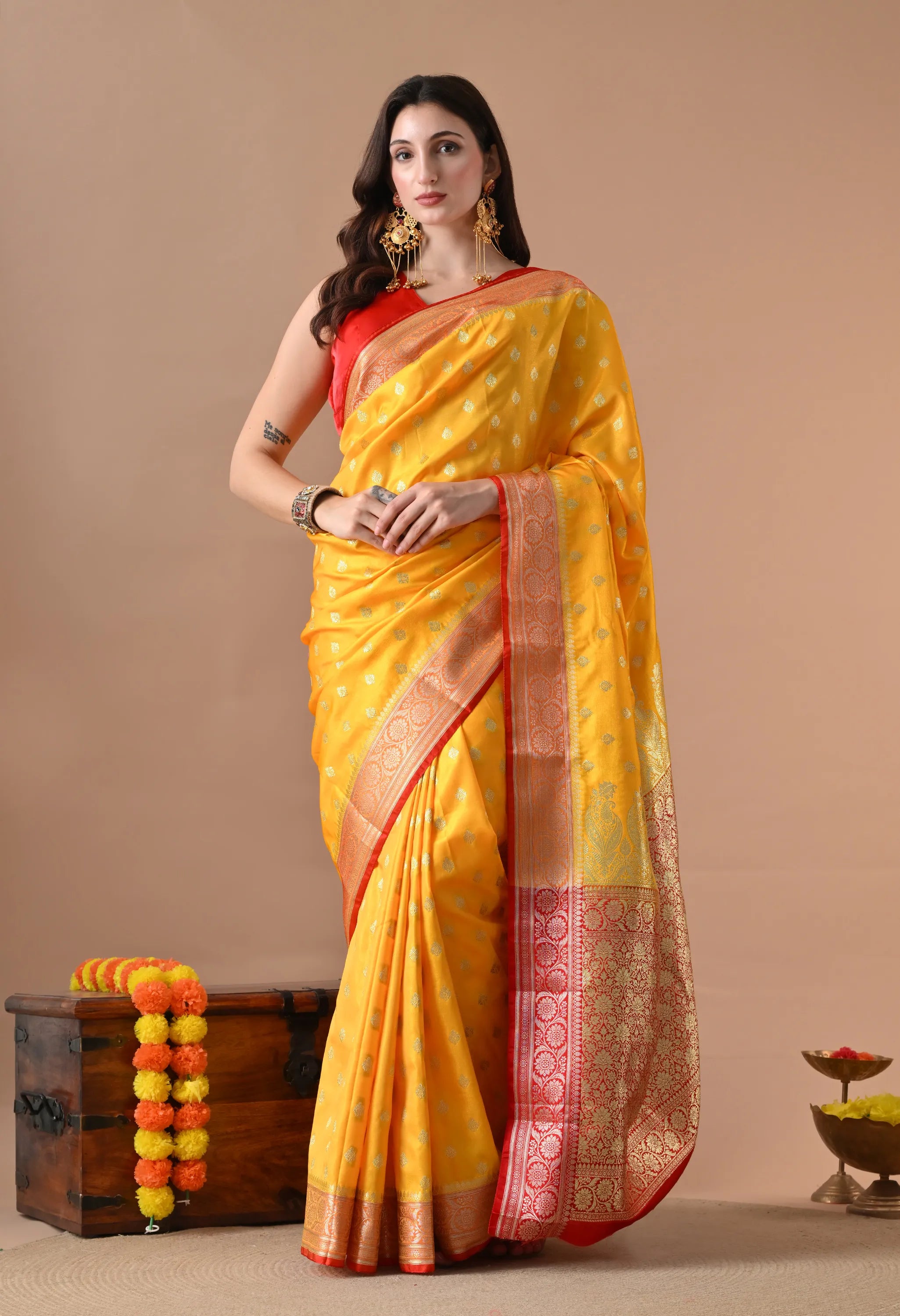 Woman posing in a bright yellow silk-blend saree with a red zari border and golden ethnic motifs.
