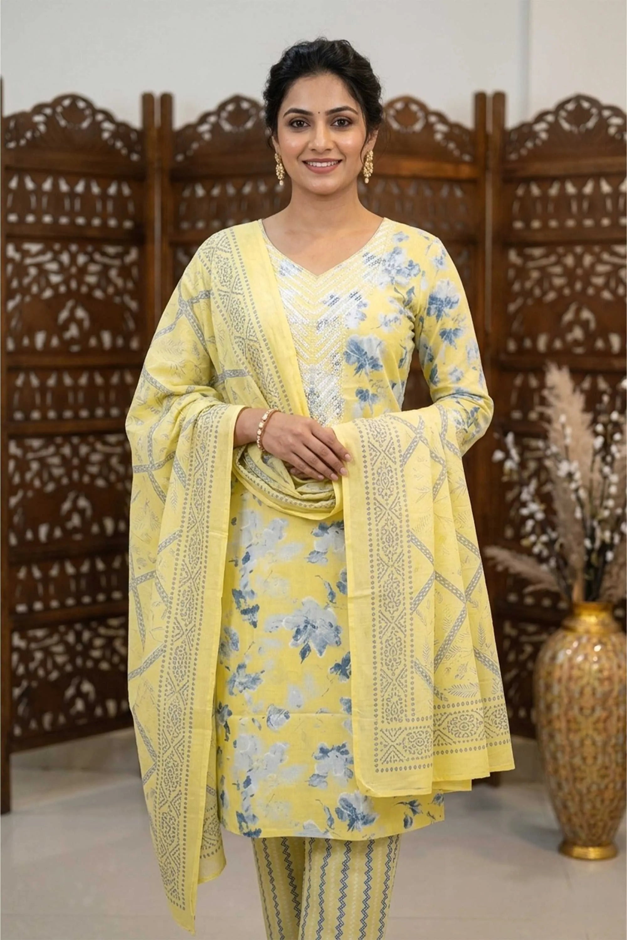 An elegant woman in a yellow and blue floral-printed cotton-blend unstitched suit with an embroidered dupatta, styled for ethnic wear.