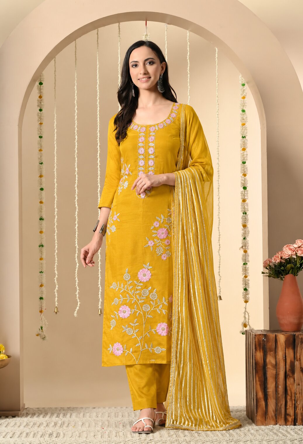 Mustard yellow kurta suit set with matching straight pants and a striped dupatta, featuring pink and white floral embroidery, a round neckline, and delicate embroidered detailing on the front.